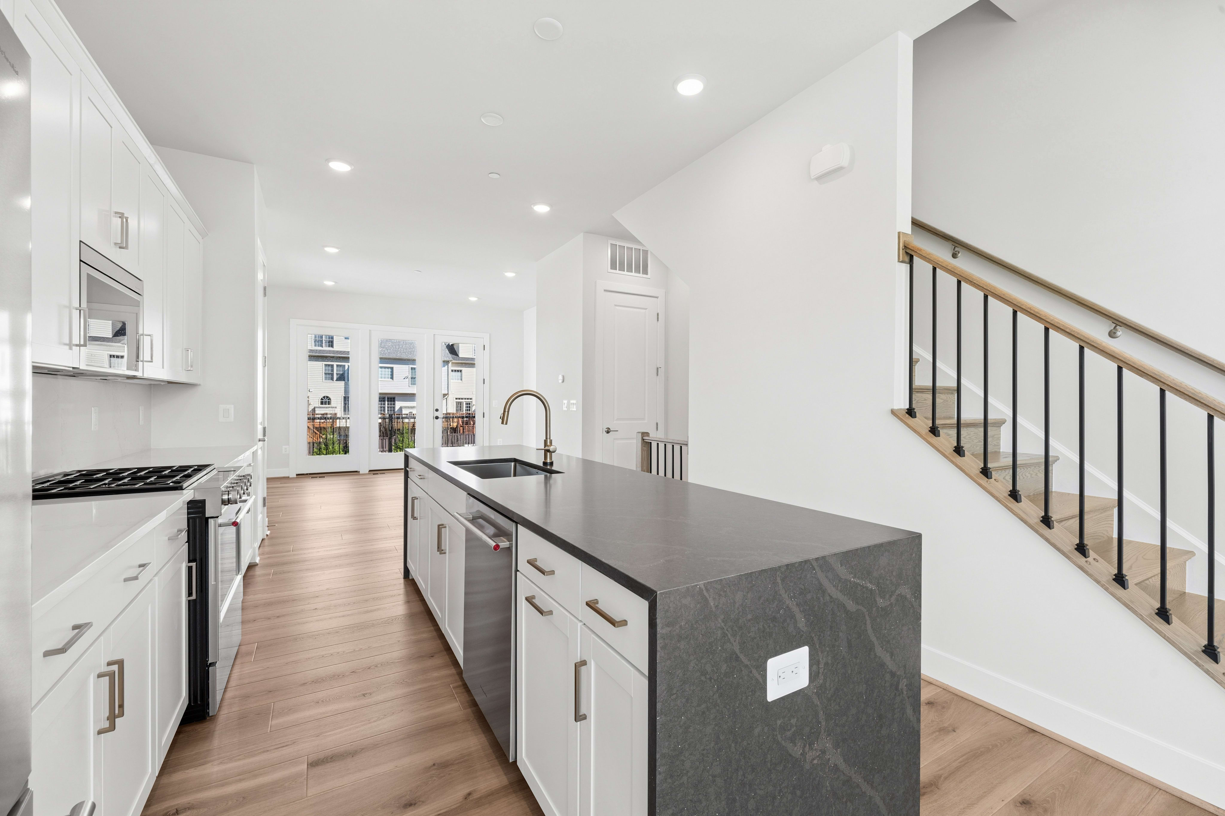 A modern kitchen with a dark gray island in the foreground and a staircase leading upstairs in the background.
