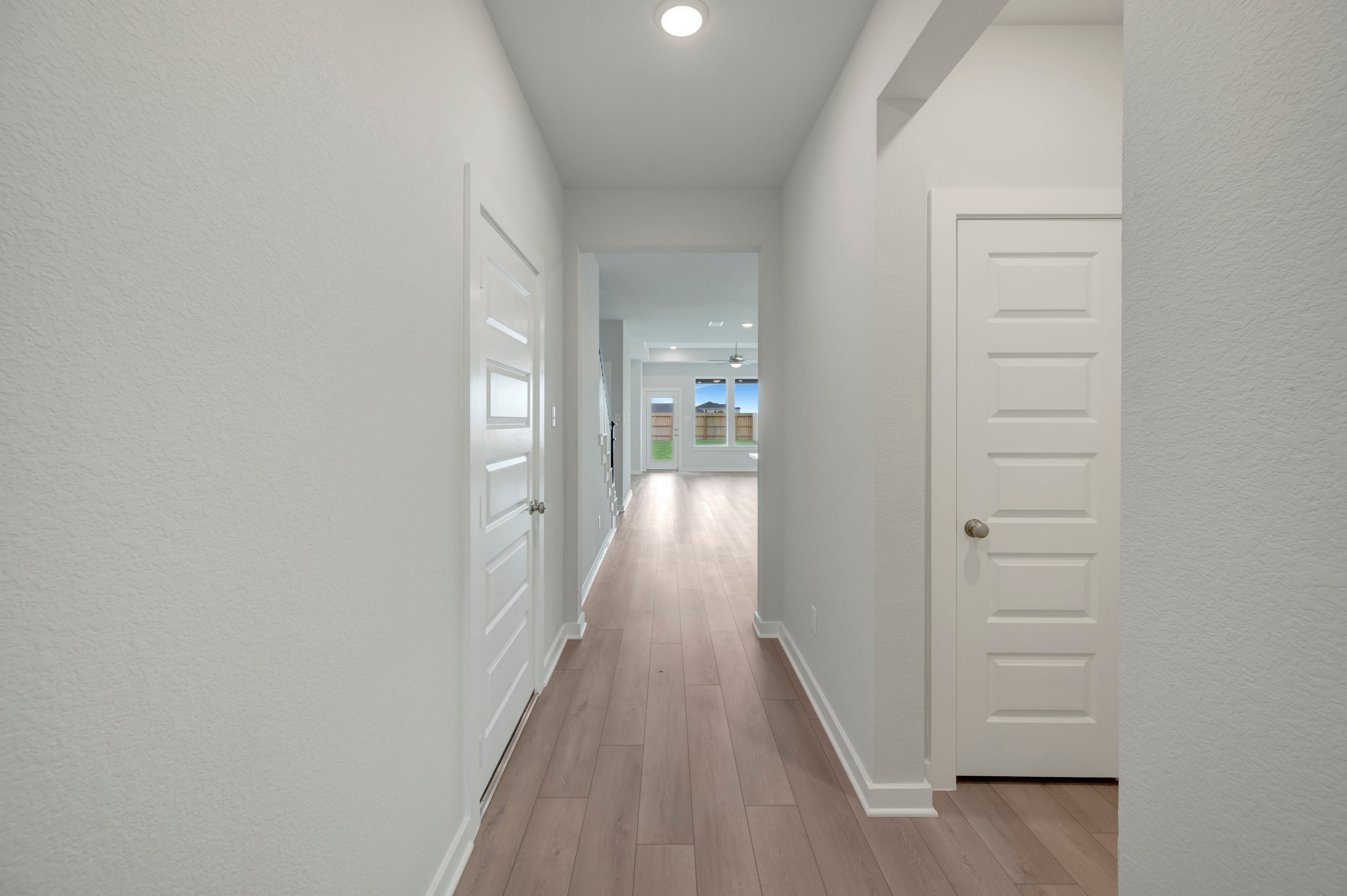 A bright, modern hallway with light wood floors leads to an open living space with large windows.