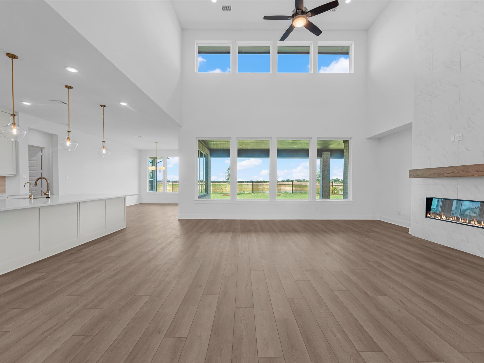 A modern, open-concept living space with a sleek white kitchen island in the foreground and a vast, green landscape visible through large windows in the background.