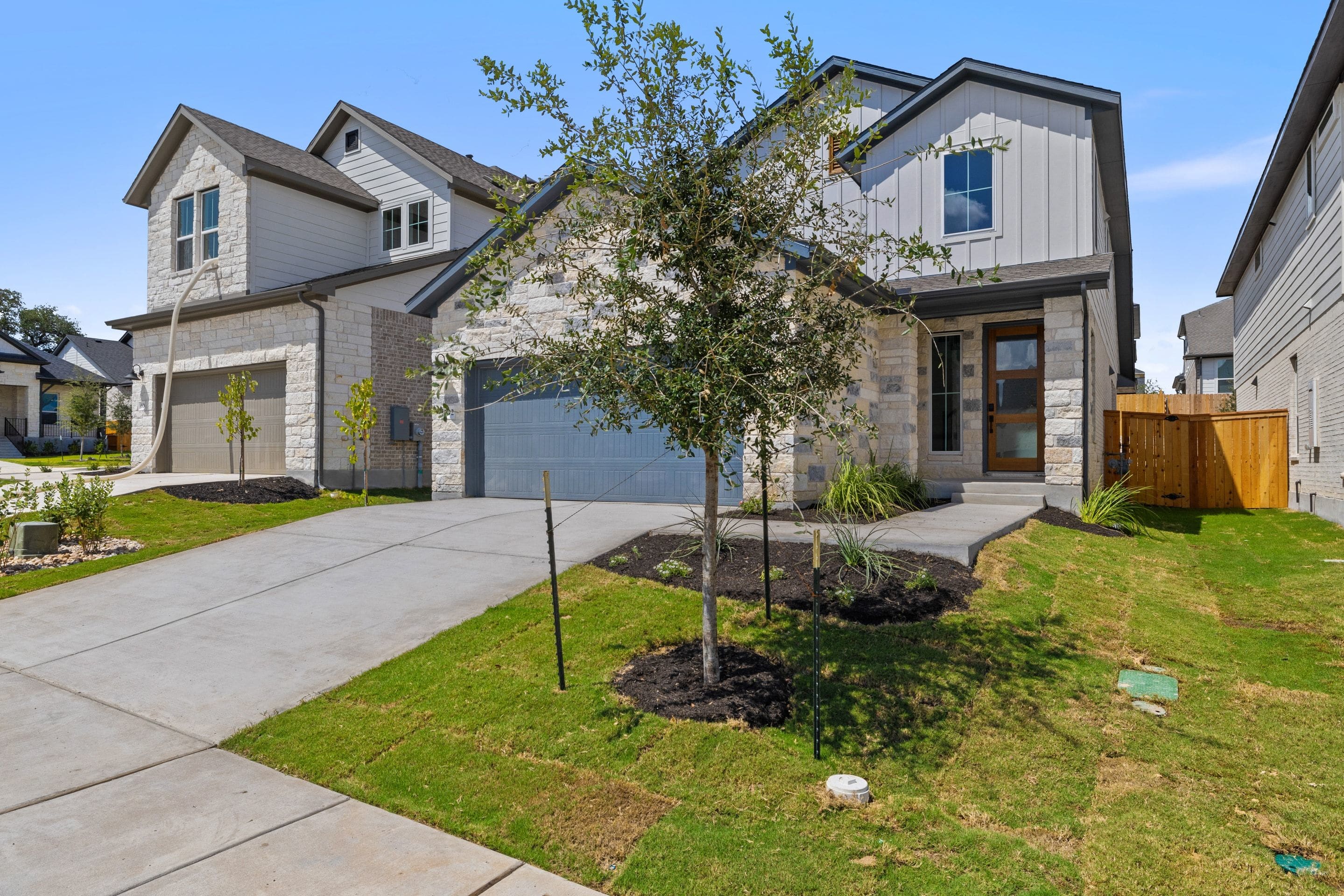 A modern stone and white-sided house with a gray garage door sits on a manicured lawn in front of a clear blue sky.