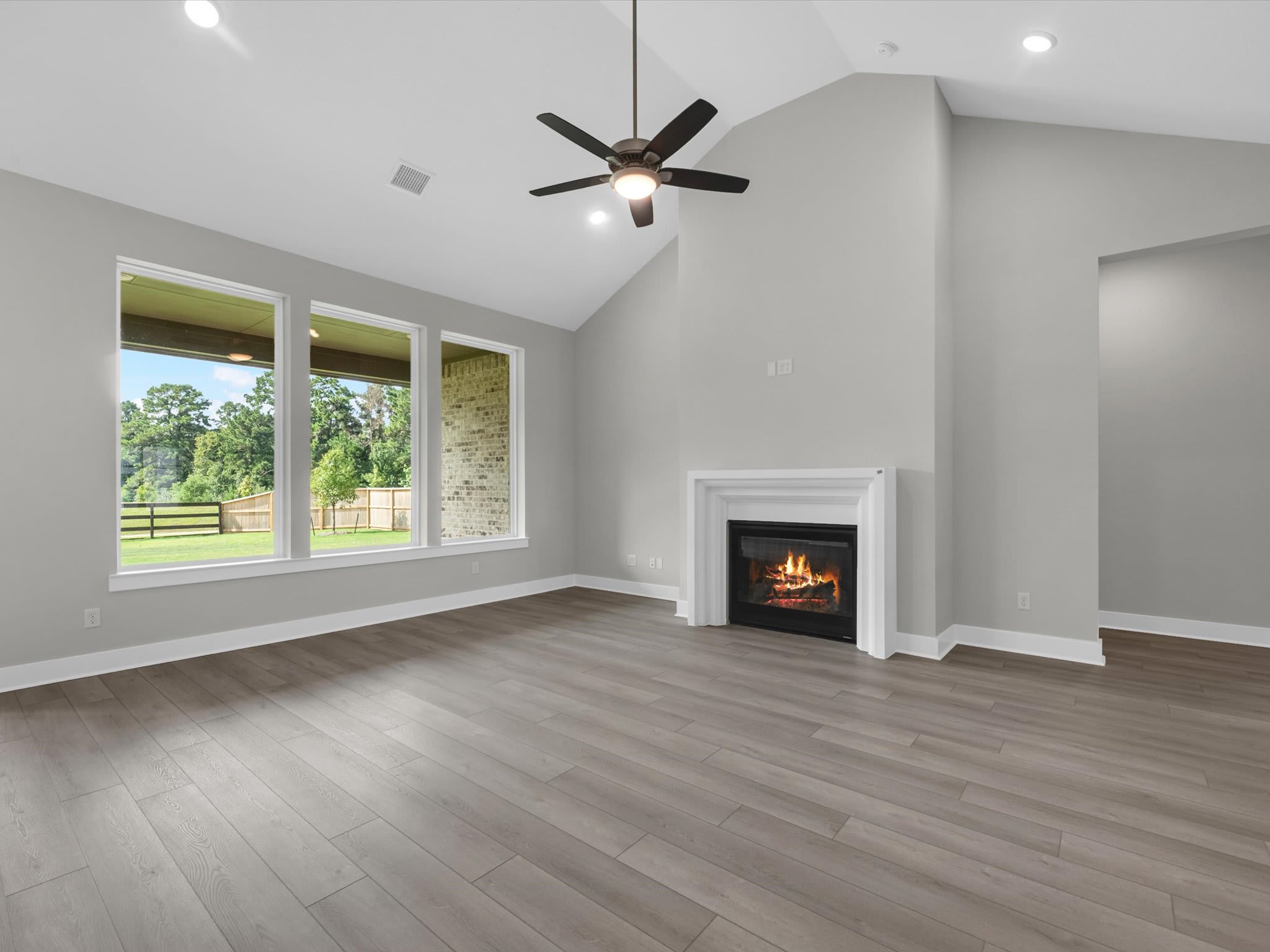A light-colored wood floor leads to a cozy fireplace and large windows overlooking a green backyard.
