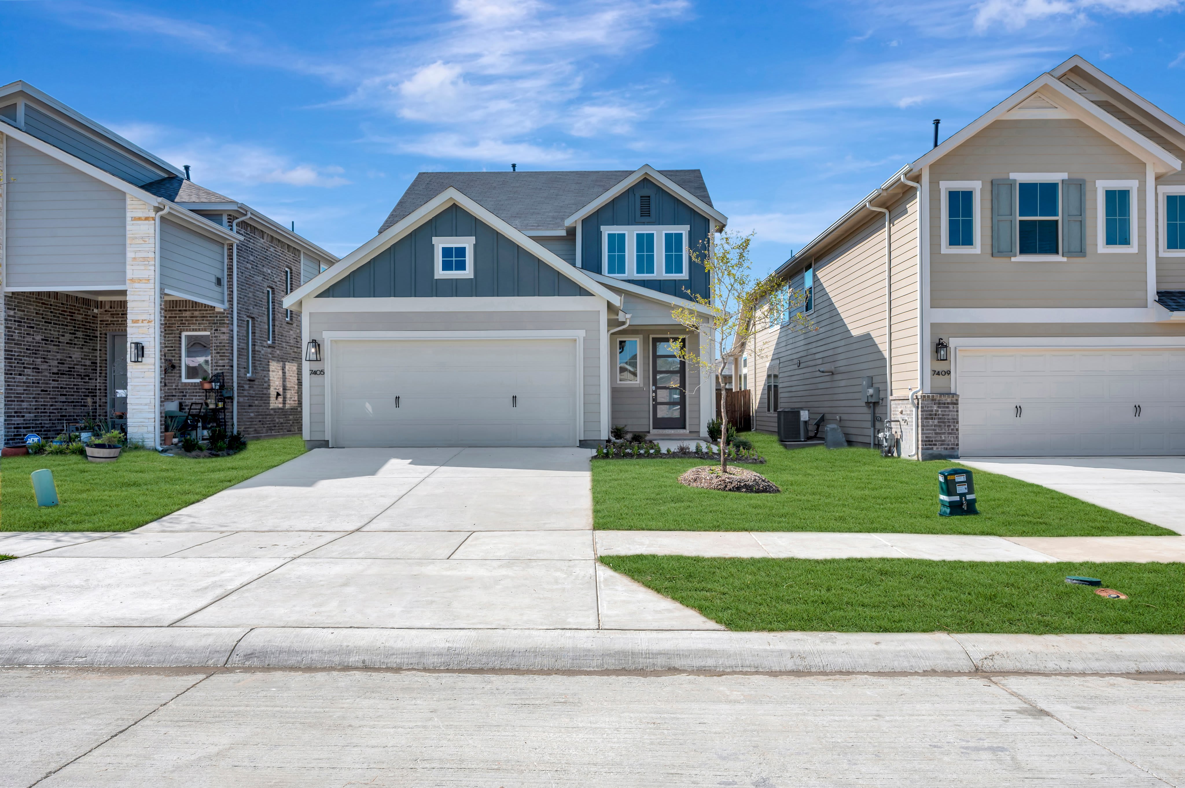 A concrete street and green lawns lead to a row of modern suburban houses under a bright blue sky.