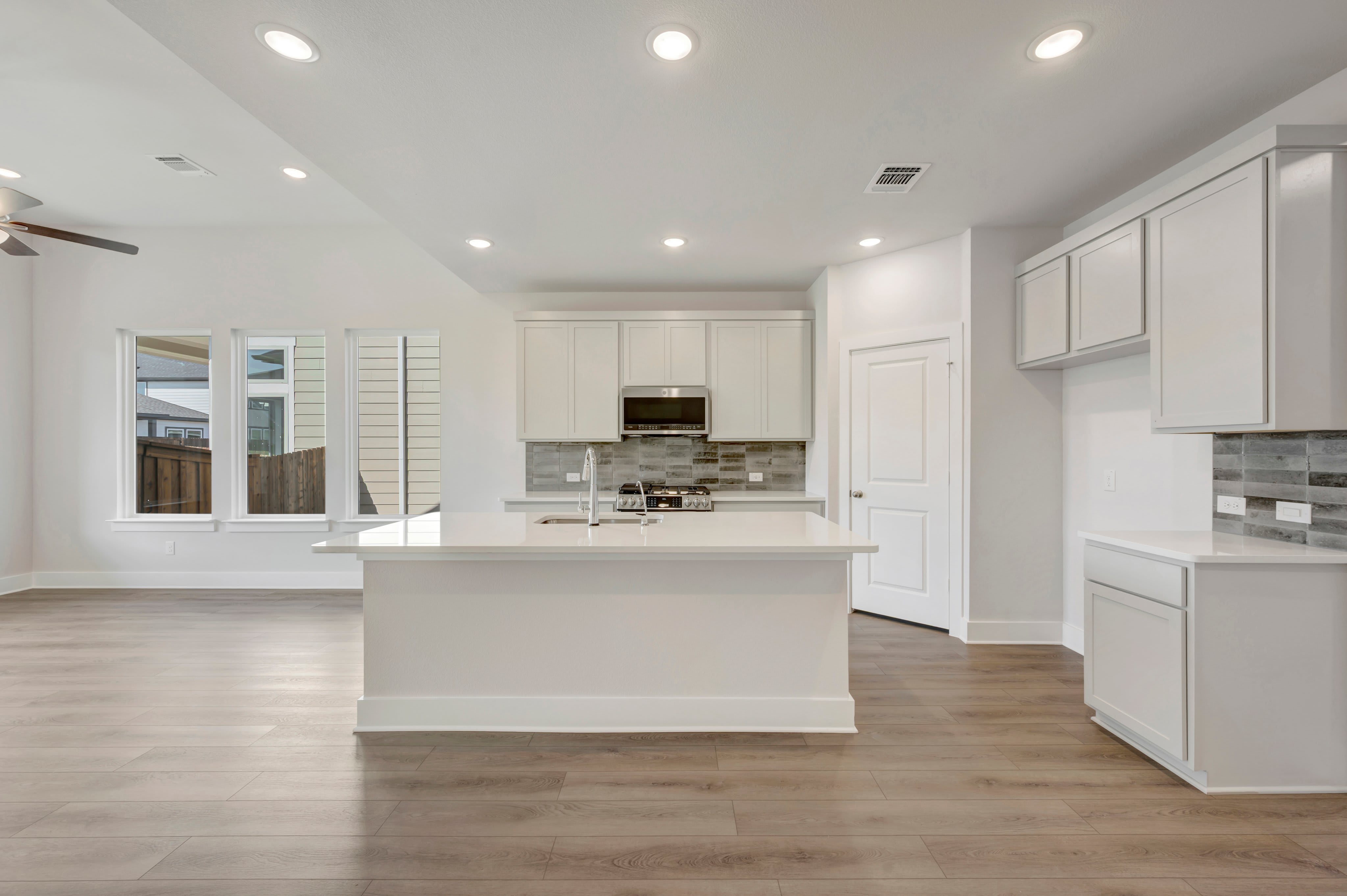 A white kitchen island sits in the foreground of a bright, modern kitchen with white cabinetry and light wood flooring.