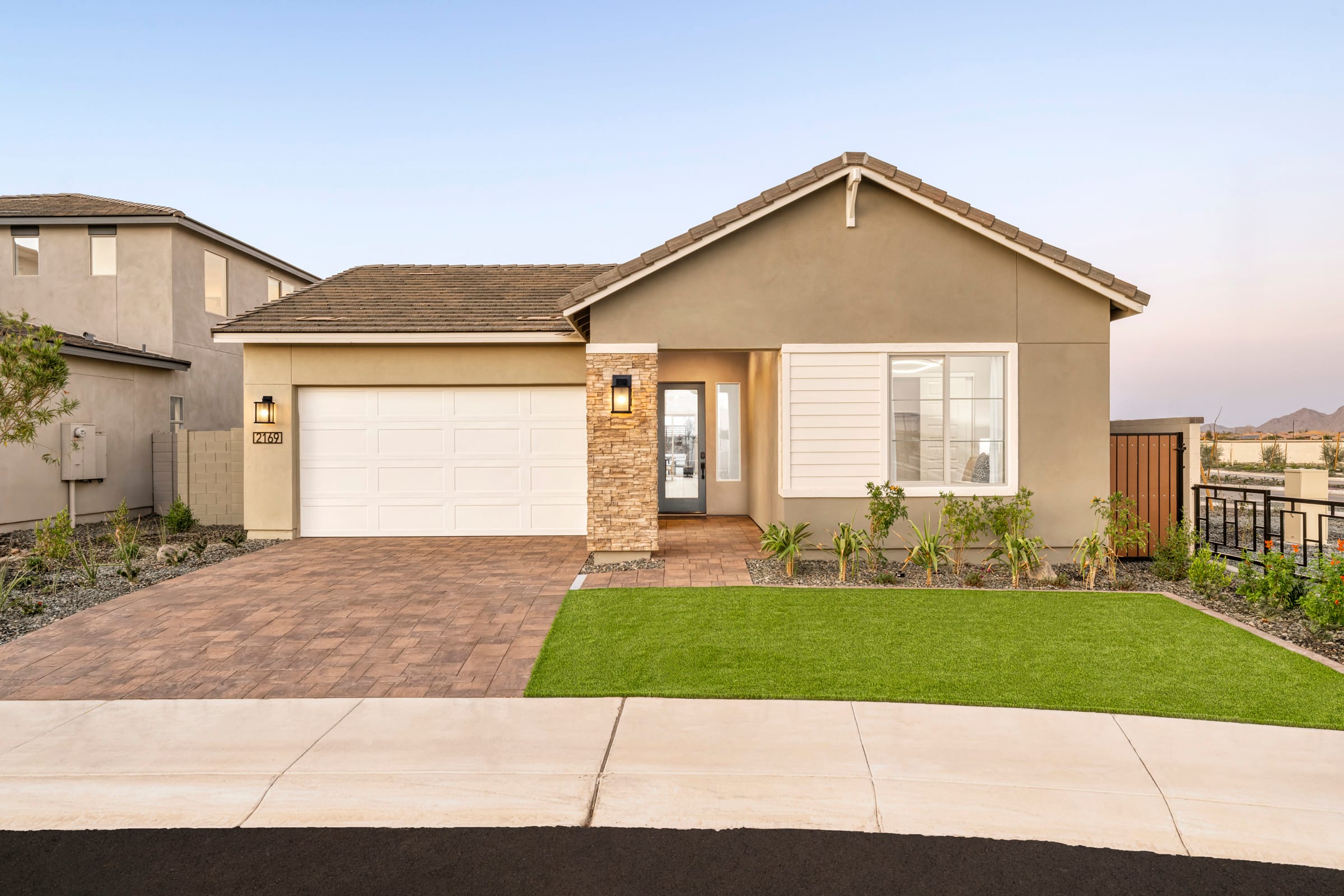 A modern single-story home with a white garage door and green lawn sits before a clear sky and distant hills.