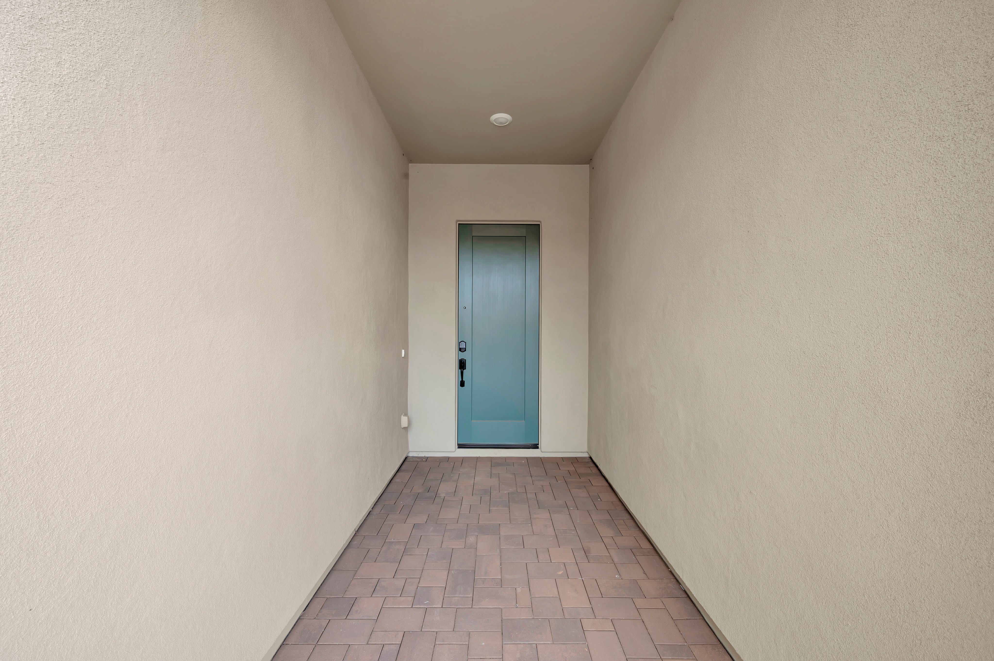 A tiled walkway leads through beige walls toward a light blue door in the background.