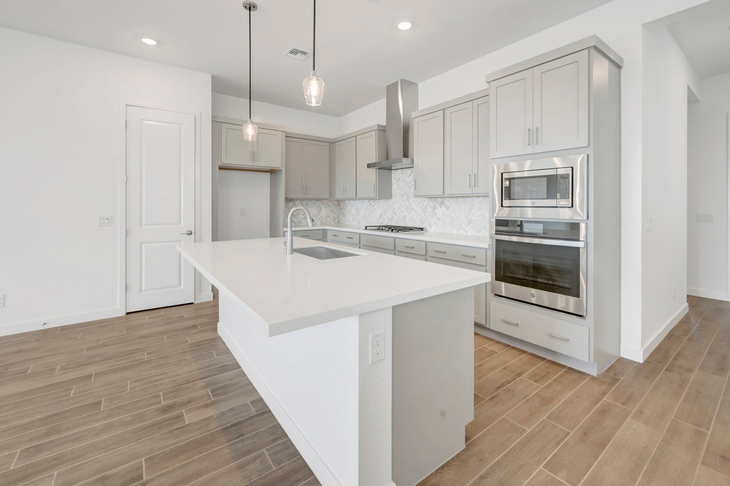 A white kitchen island with a sink sits in the foreground of a modern kitchen featuring grey cabinetry and stainless steel appliances in the background.
