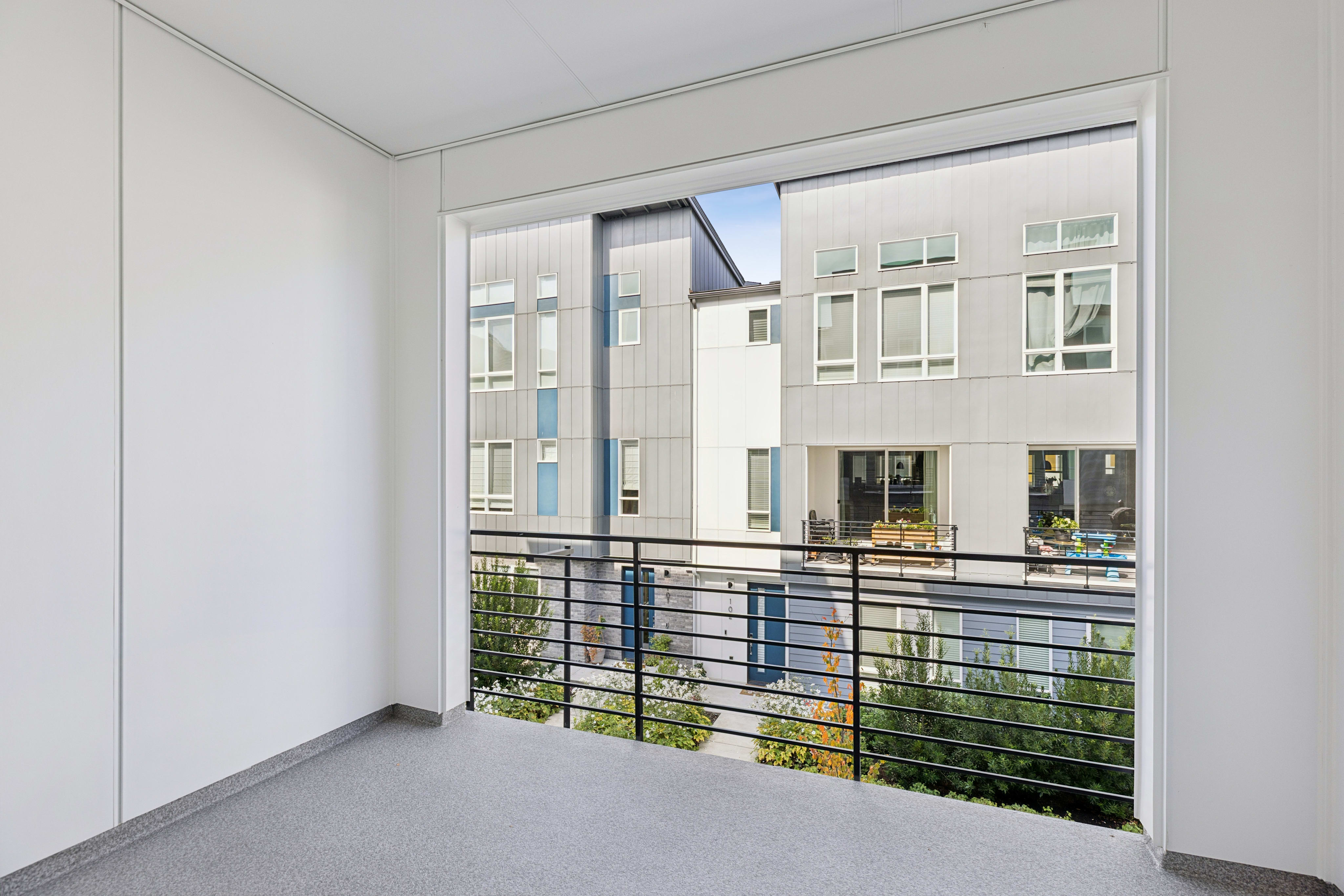 A grey-floored balcony with a black metal railing overlooks a modern multi-story apartment complex.
