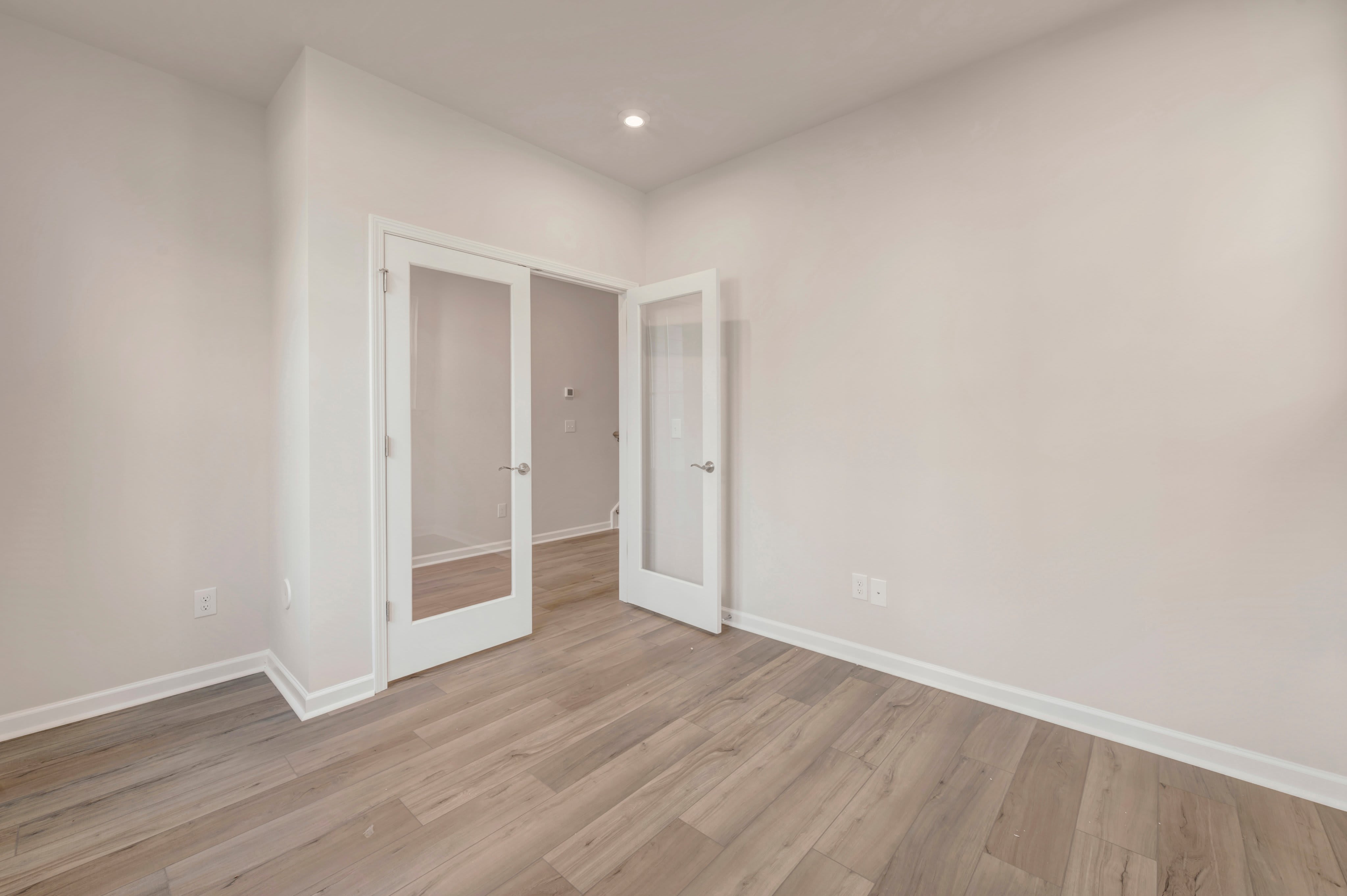 Light-colored hardwood floors lead toward a set of open white French doors that reveal another empty room in the background.