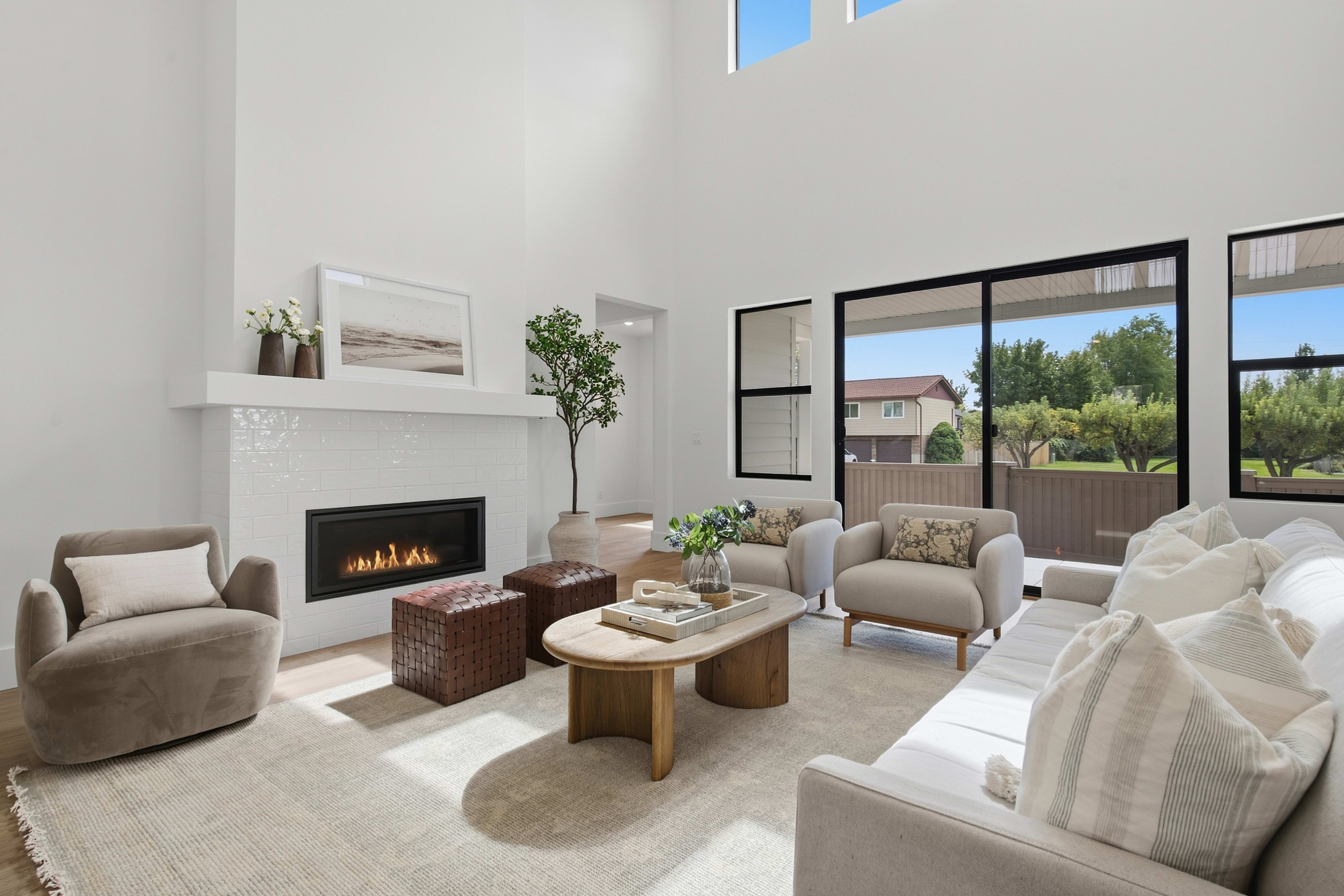 A modern living room features a neutral-toned seating area with a wooden coffee table in the foreground and a white fireplace against a high wall in the background.