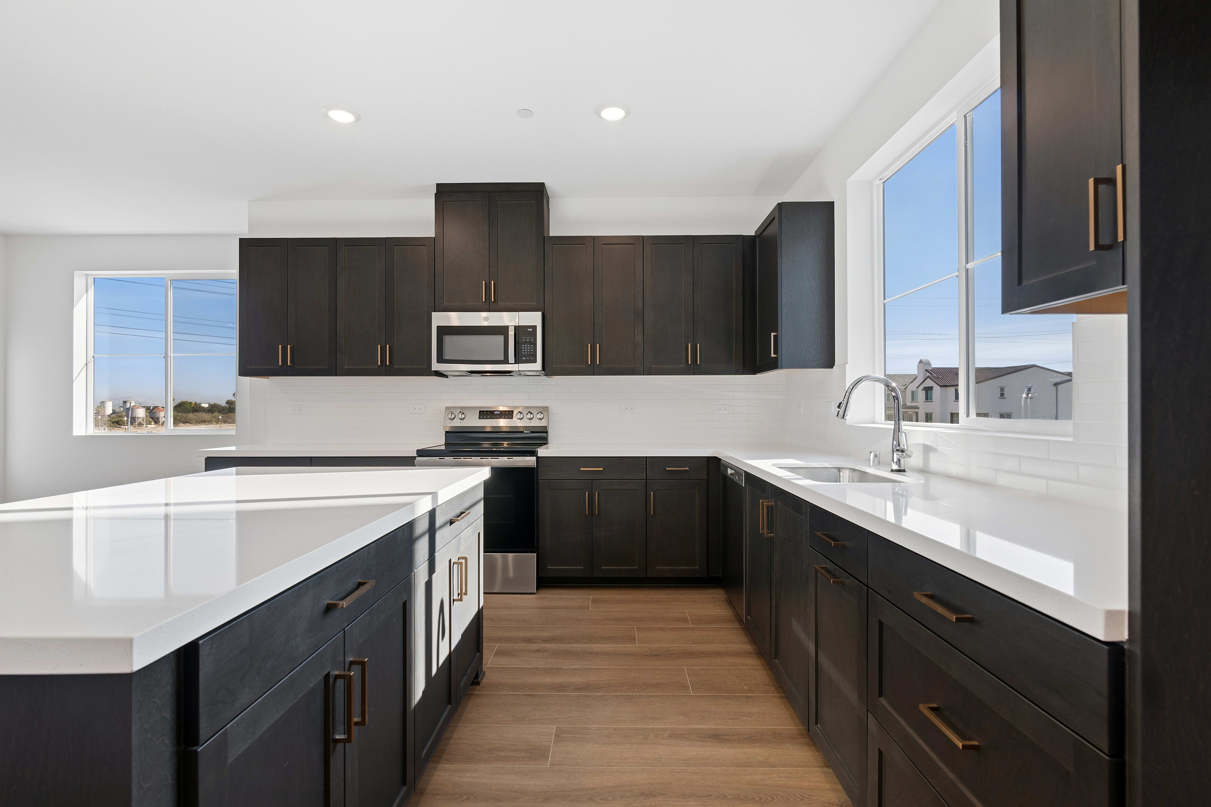 A modern kitchen features a white quartz island in the foreground and dark wood cabinetry with stainless steel appliances against a white wall in the background.