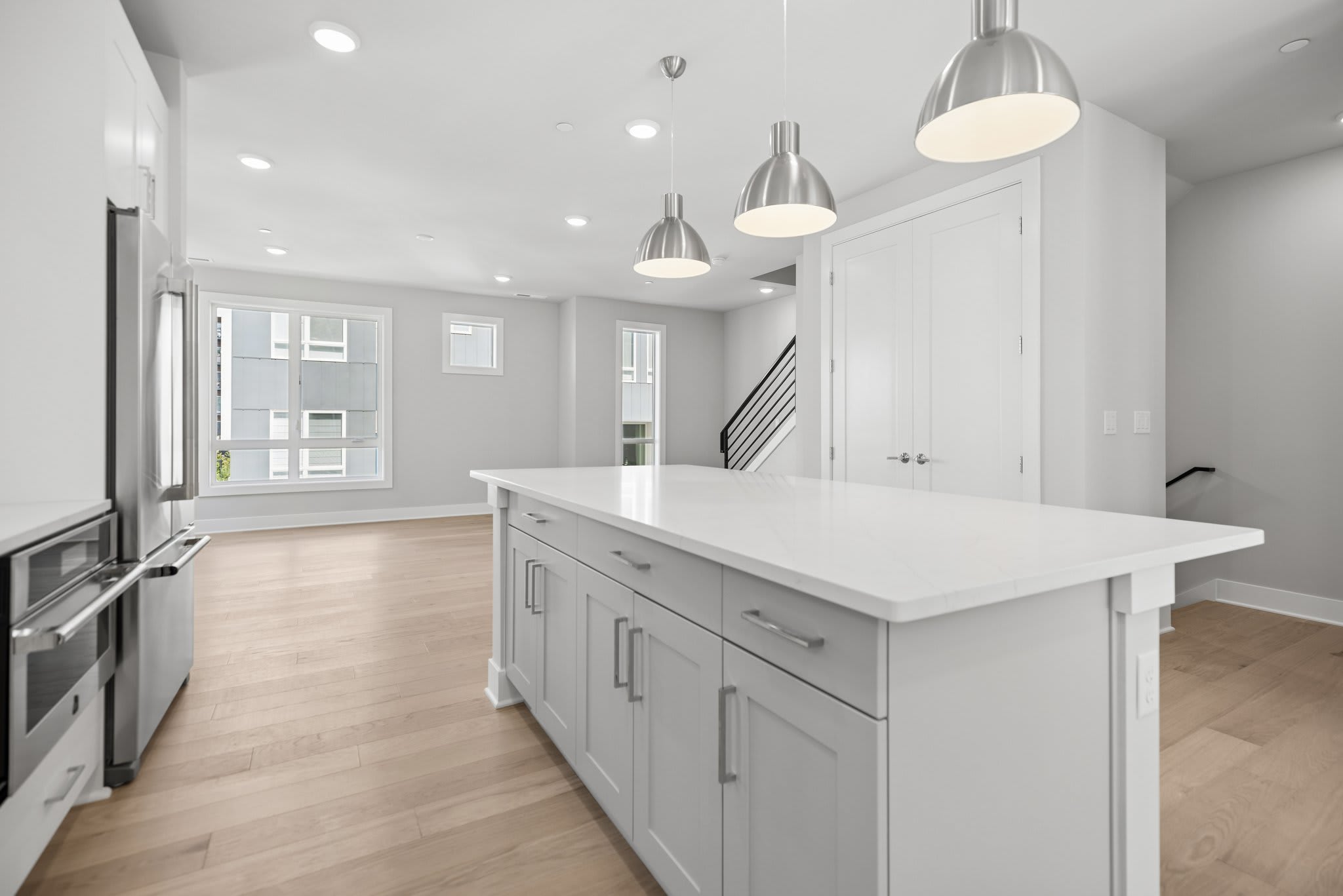 A white kitchen island with a marble countertop sits in the foreground of a bright, open-concept room featuring light wood floors and a staircase in the background.