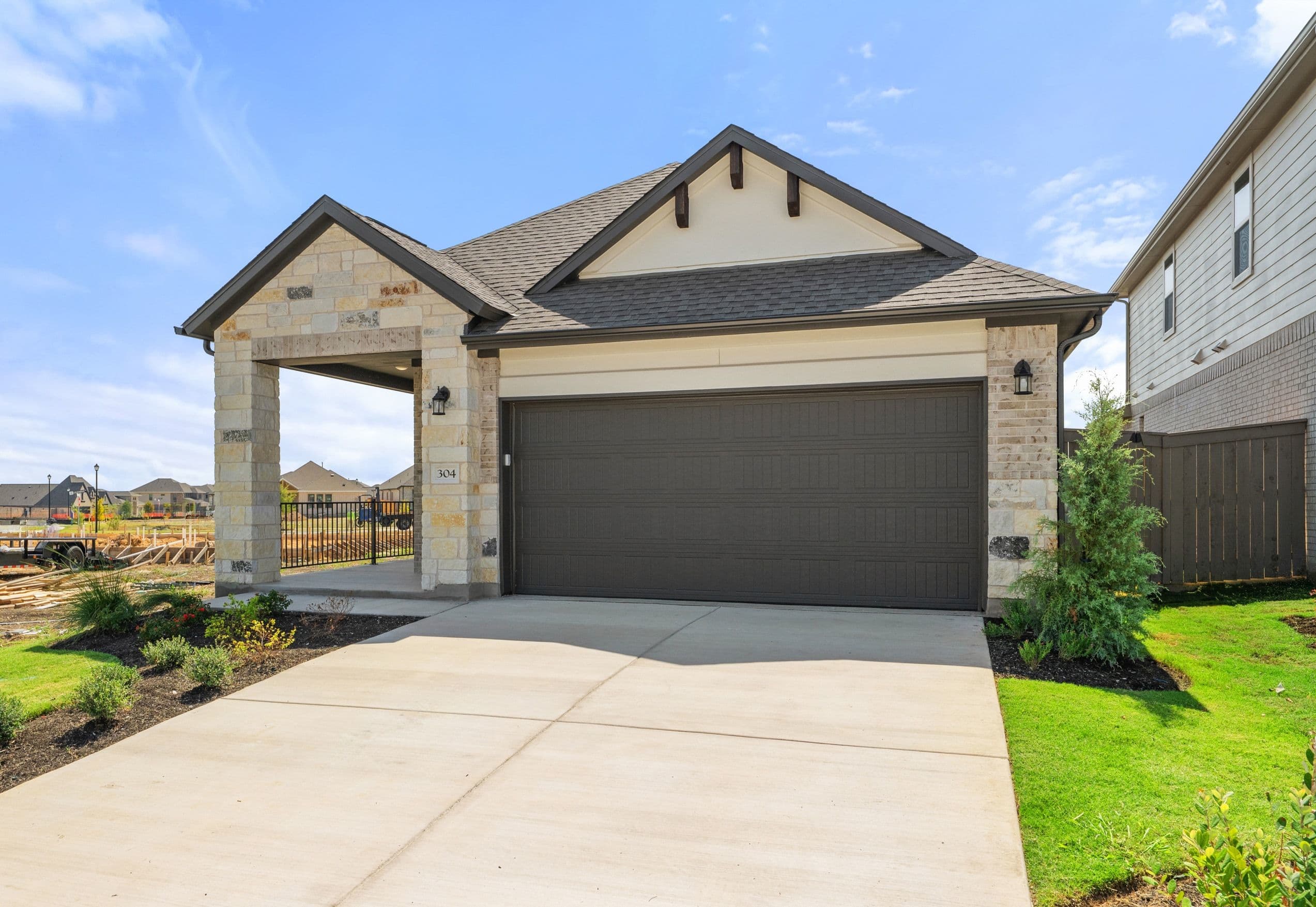 A concrete driveway leads to a modern stone house with a dark grey garage door under a bright blue sky.