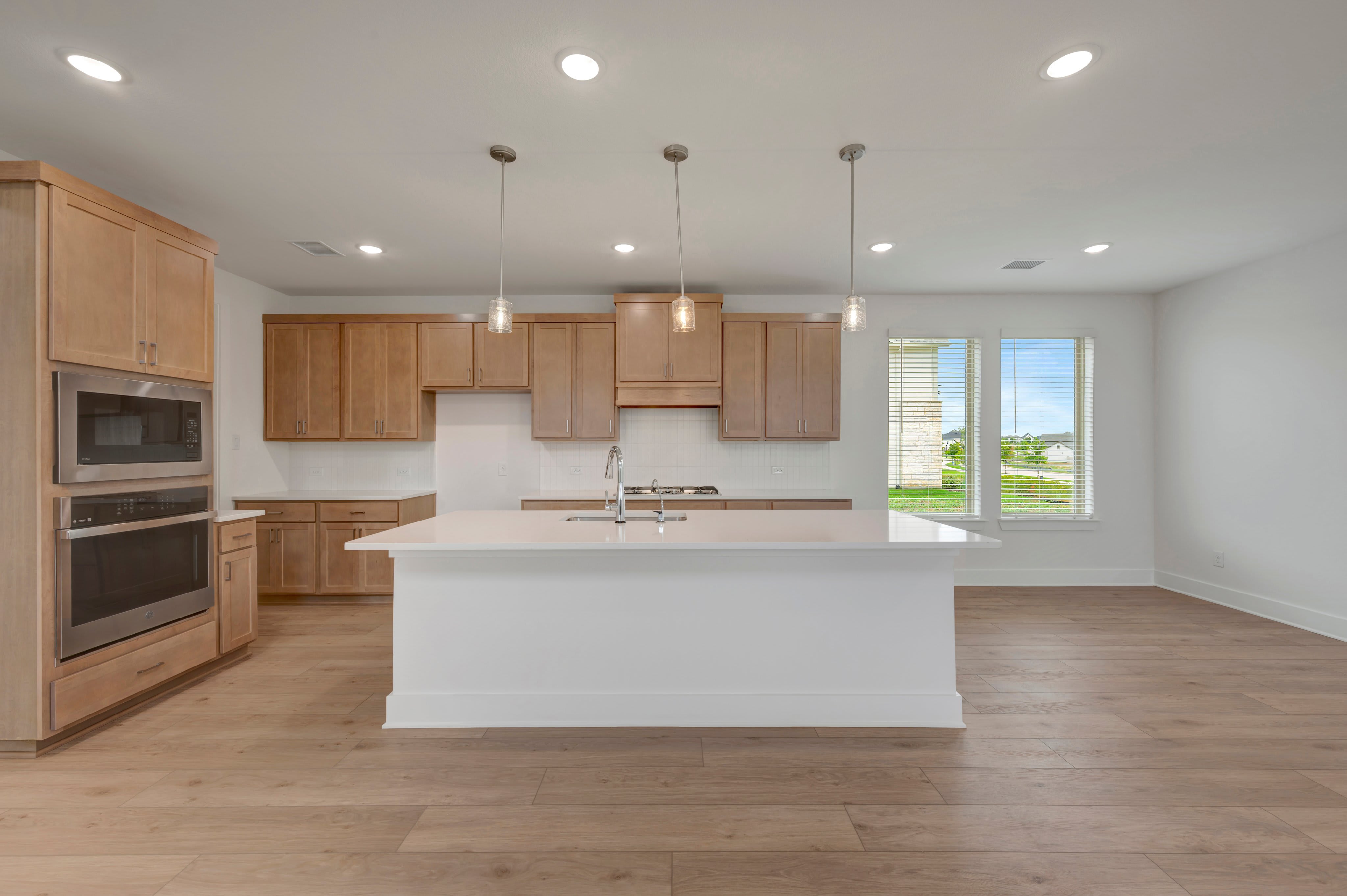 A white kitchen island sits in the foreground of a modern room with light wood cabinetry and a window in the background.