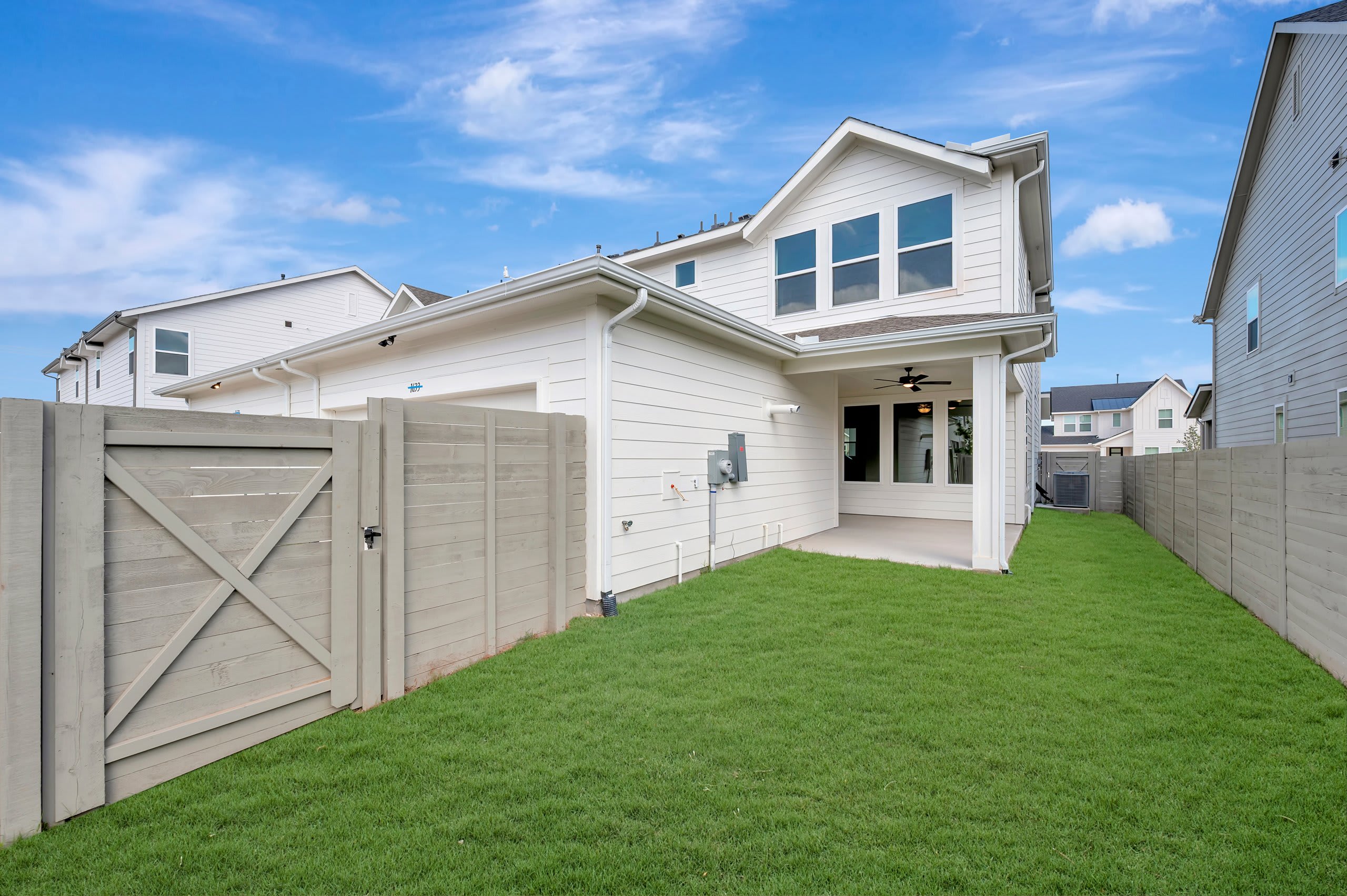A green grassy backyard is enclosed by a light-colored fence in the foreground, with a white two-story house and a blue sky in the background.