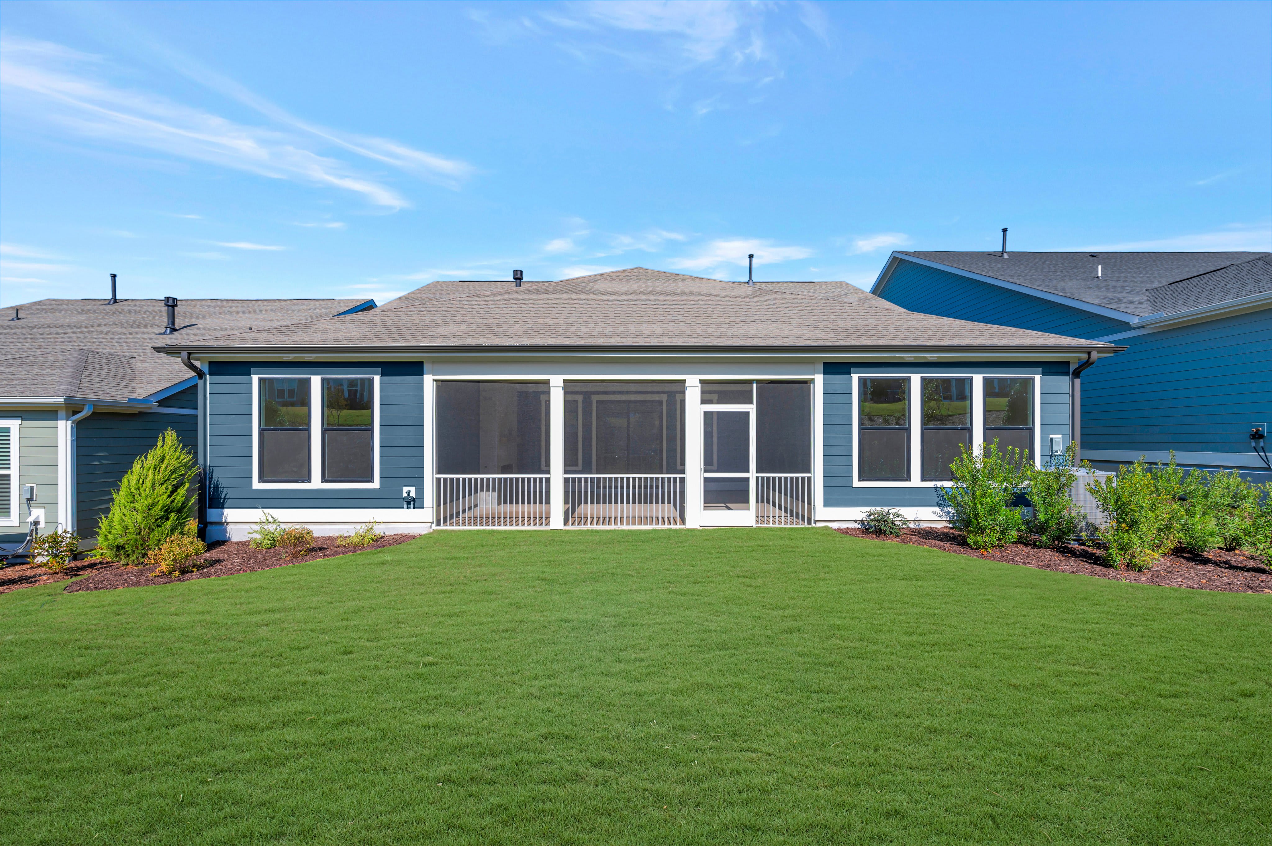 A lush green lawn fills the foreground, leading to a blue house with a screened-in porch under a bright blue sky.
