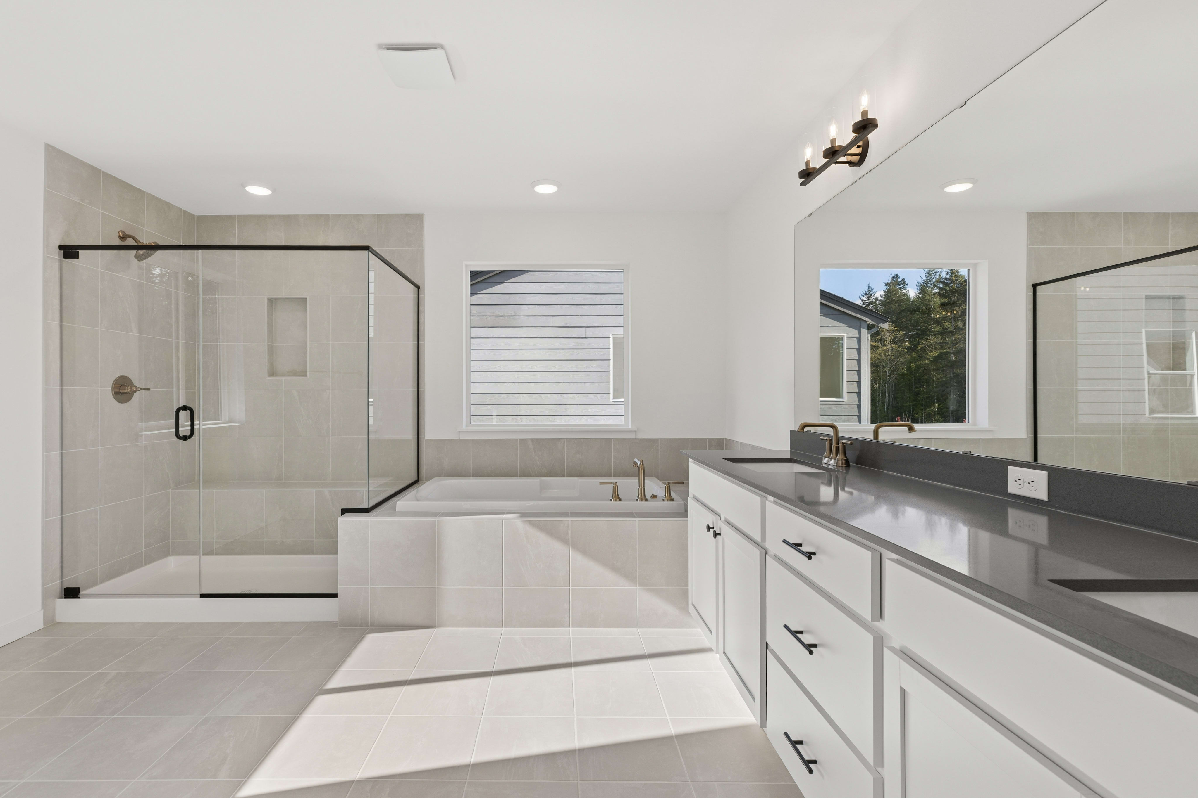 A modern bathroom features a white vanity with a grey countertop in the foreground, with a glass shower and a built-in bathtub in the background.