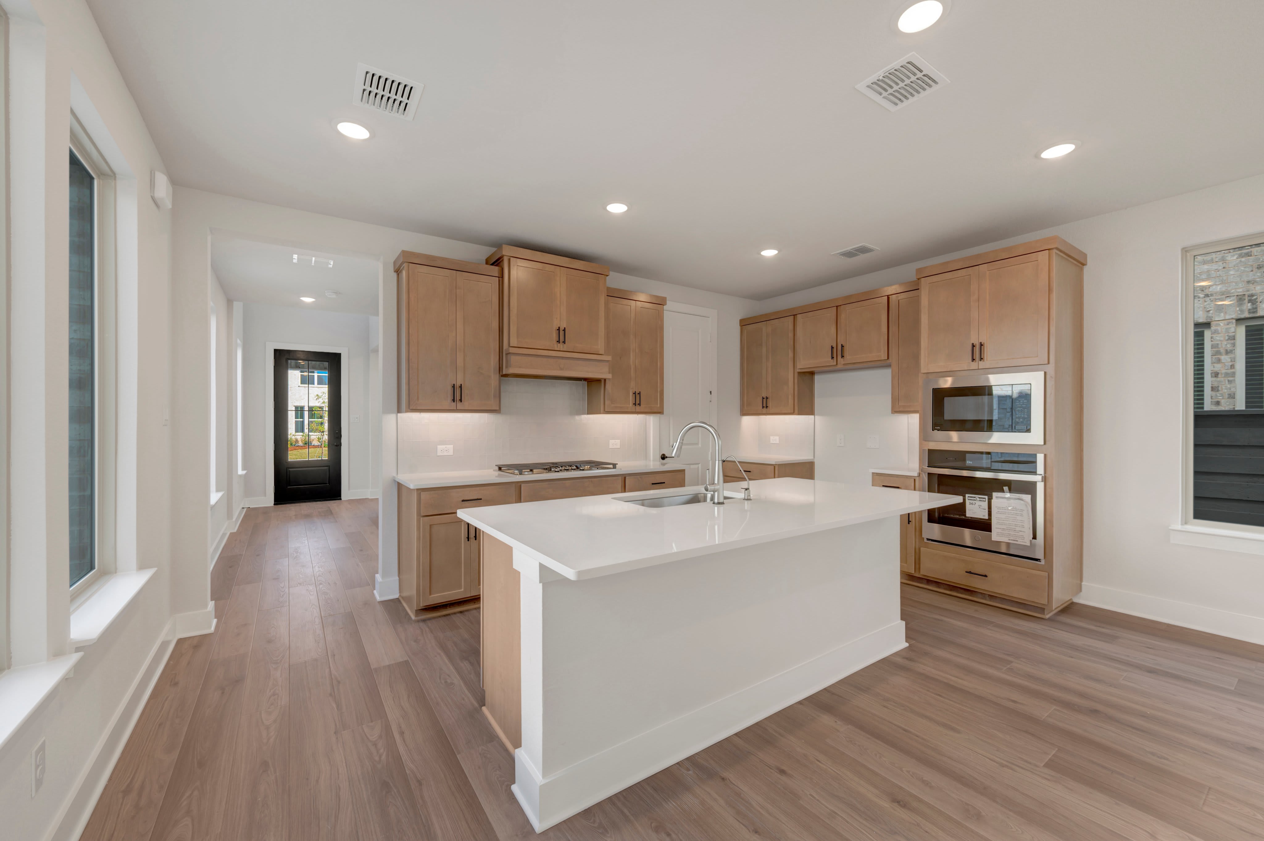 A white kitchen island sits in the foreground of a modern kitchen featuring light wood cabinetry and hardwood floors.