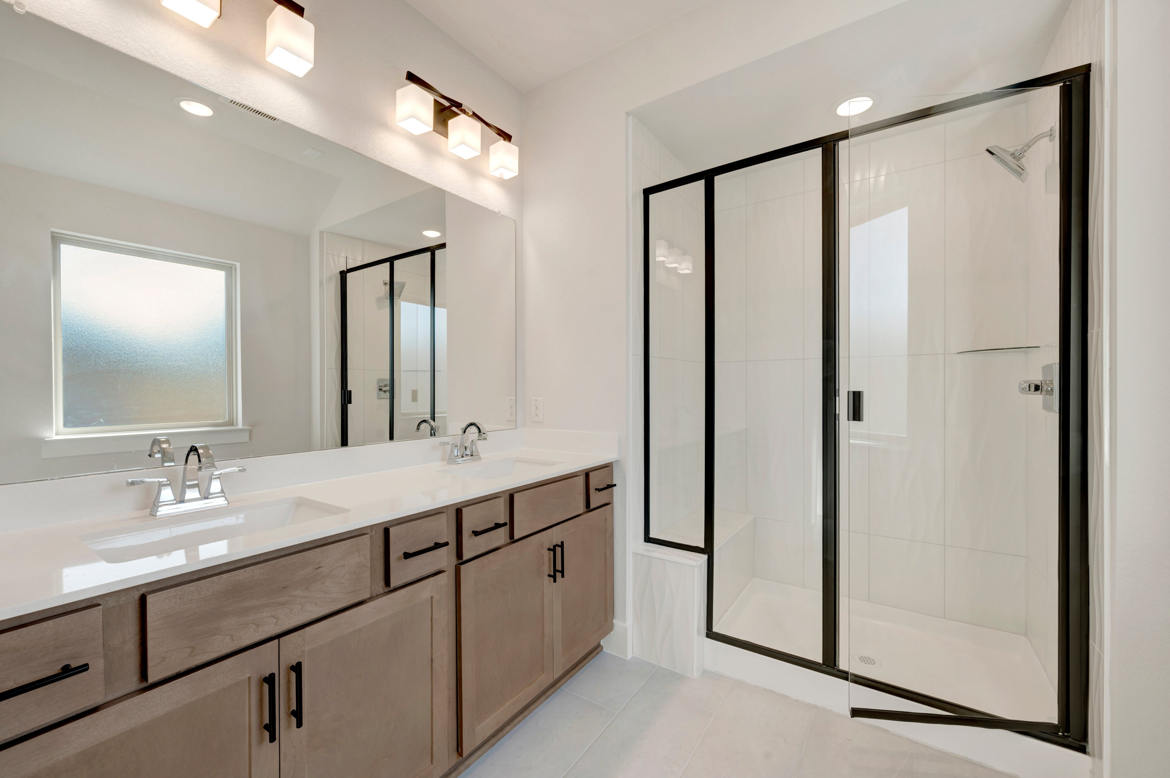 A modern bathroom features a wooden vanity with a white countertop in the foreground and a glass-enclosed shower in the background.