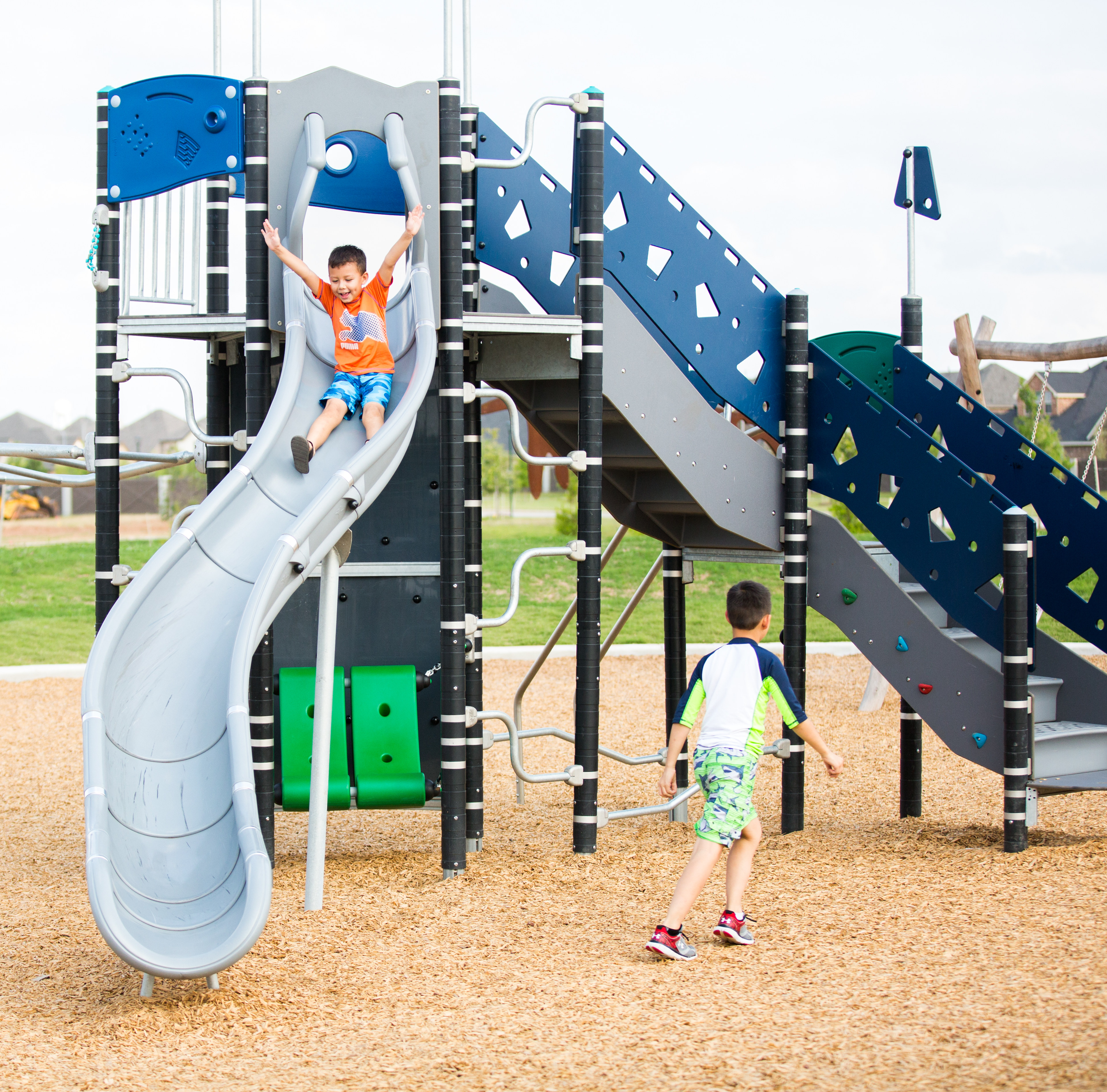 A colorful and modern playground with various slides, climbing structures, and a child playing on the equipment in the foreground.