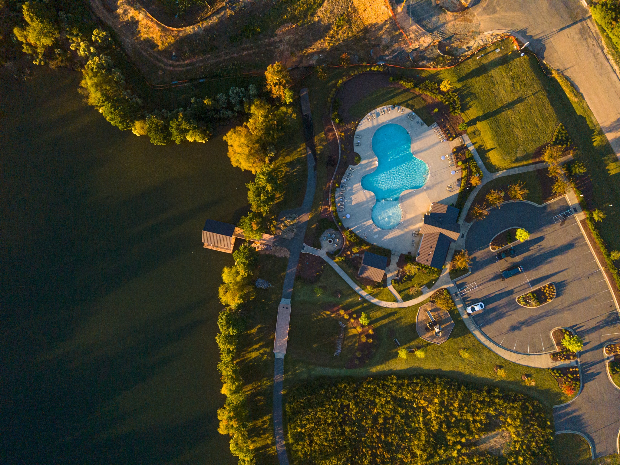 An aerial view of a scenic landscape with a large swimming pool surrounded by lush greenery, buildings, and a winding road.