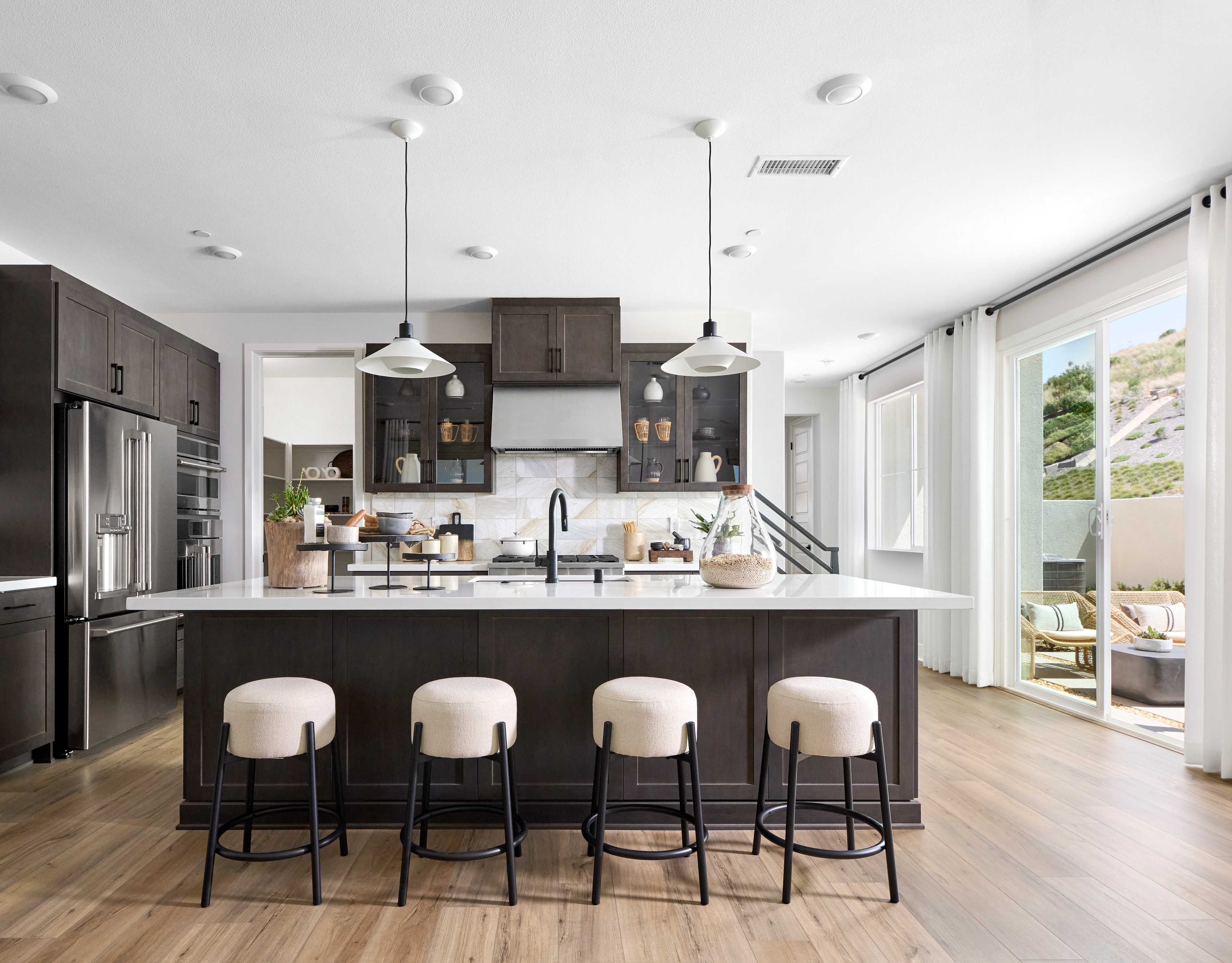 A modern and sleek kitchen with dark cabinets, a large island with bar stools, and a bright and airy atmosphere with large windows.