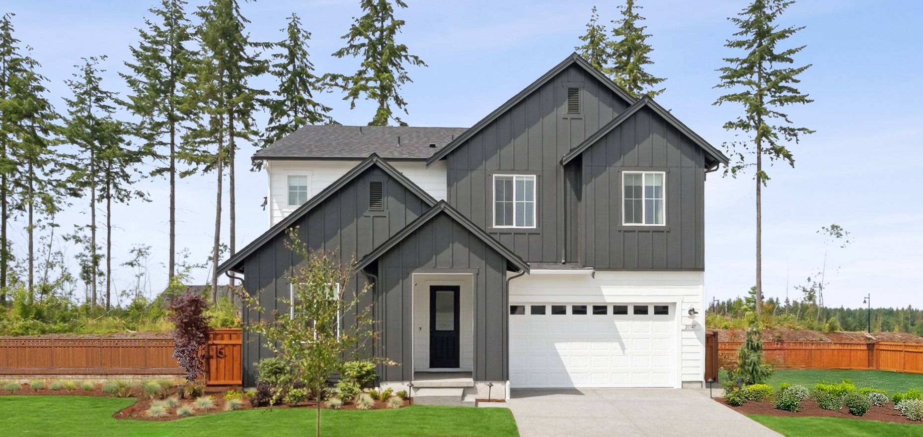 A modern, two-story house with a gray exterior and a white trim, surrounded by lush greenery and a well-manicured lawn in the foreground.