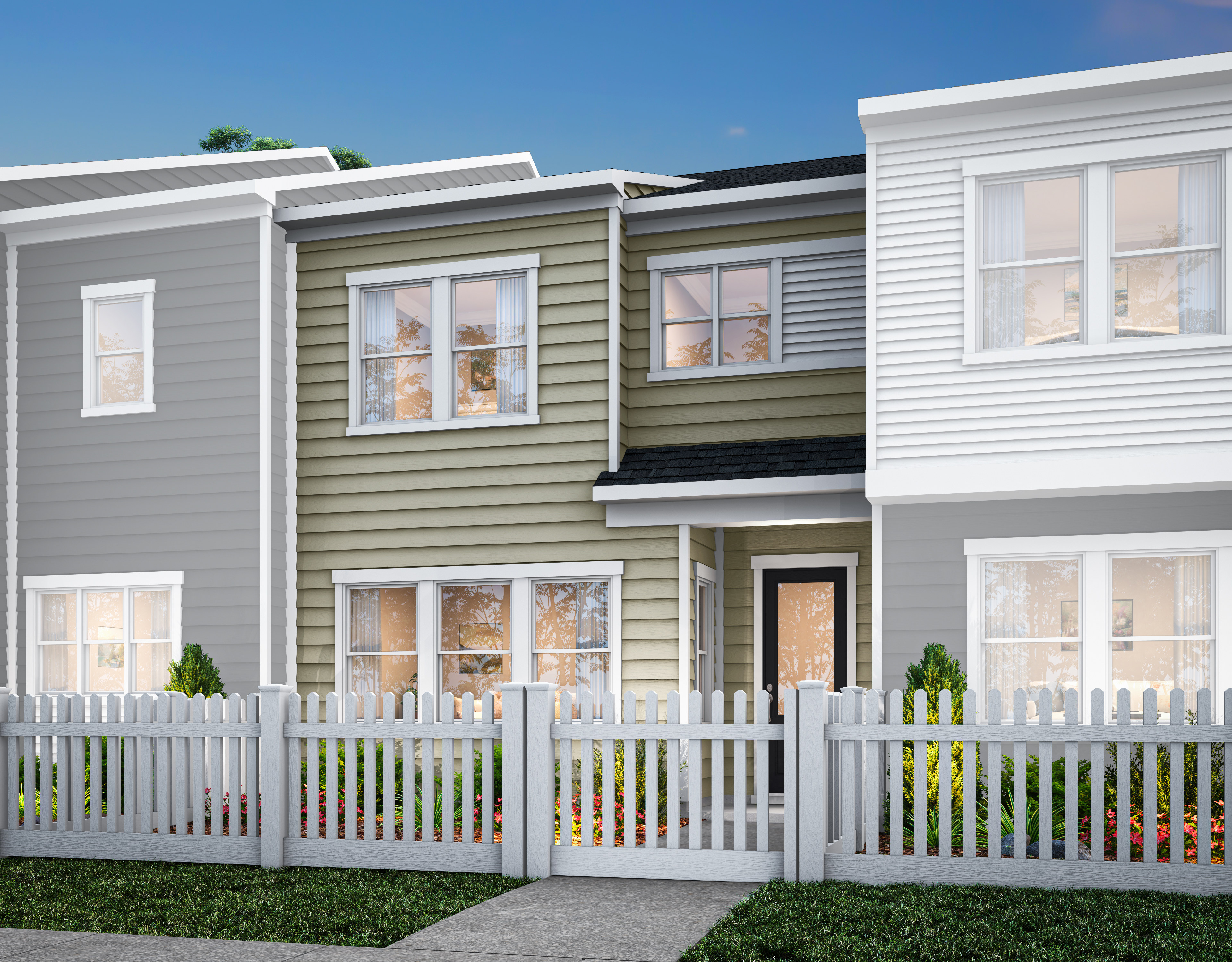 A row of modern, multi-story townhouses with gray and green siding, white trim, and a white picket fence in the foreground, set against a clear blue sky.