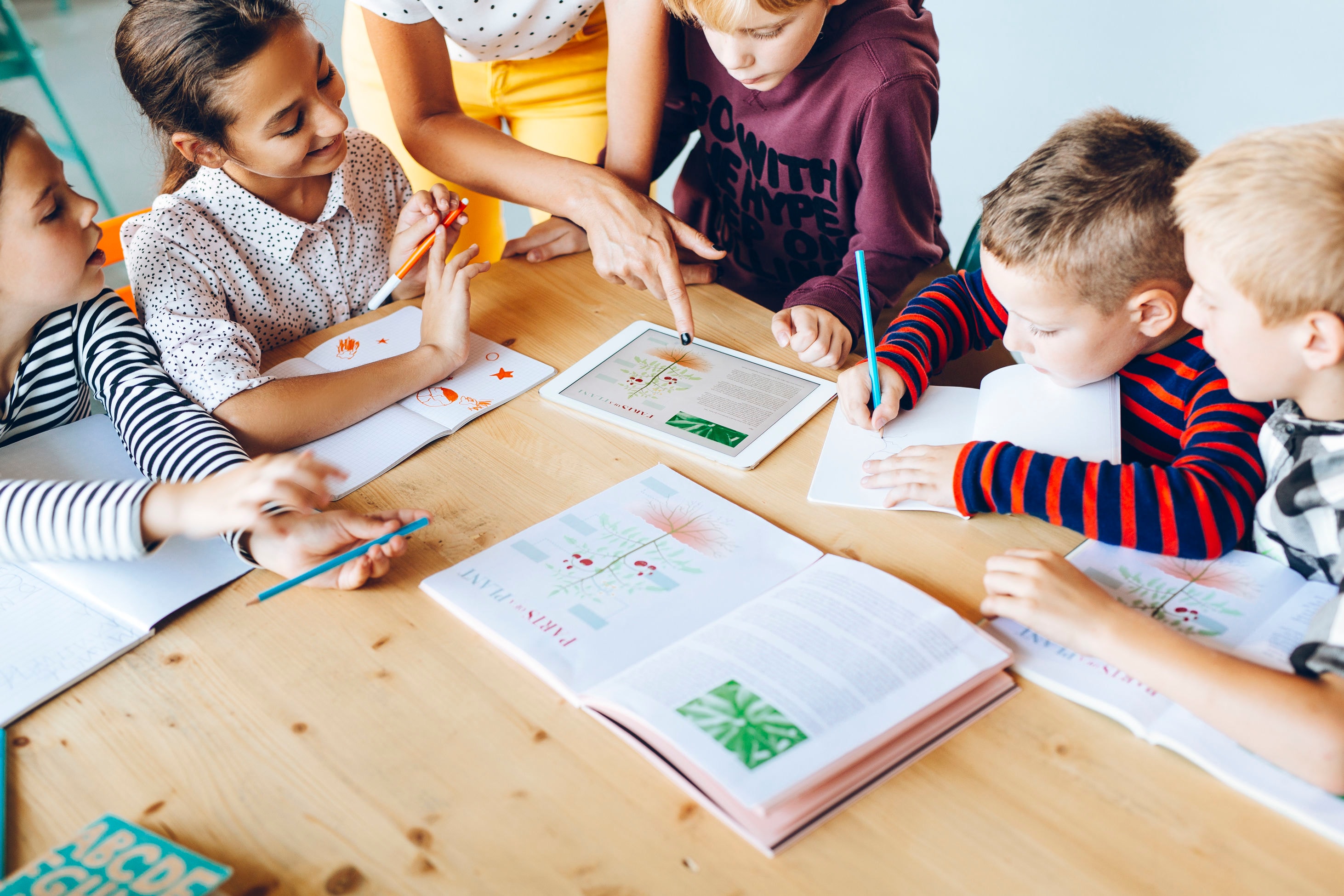 A group of young students are gathered around a table, engaged in a collaborative learning activity, with various educational materials and supplies visible on the table.