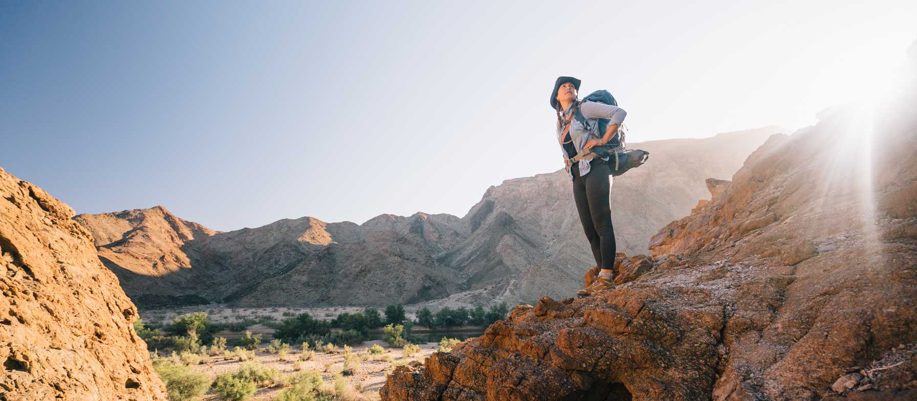 A person stands atop a rocky cliff, overlooking a vast, mountainous landscape in the background.