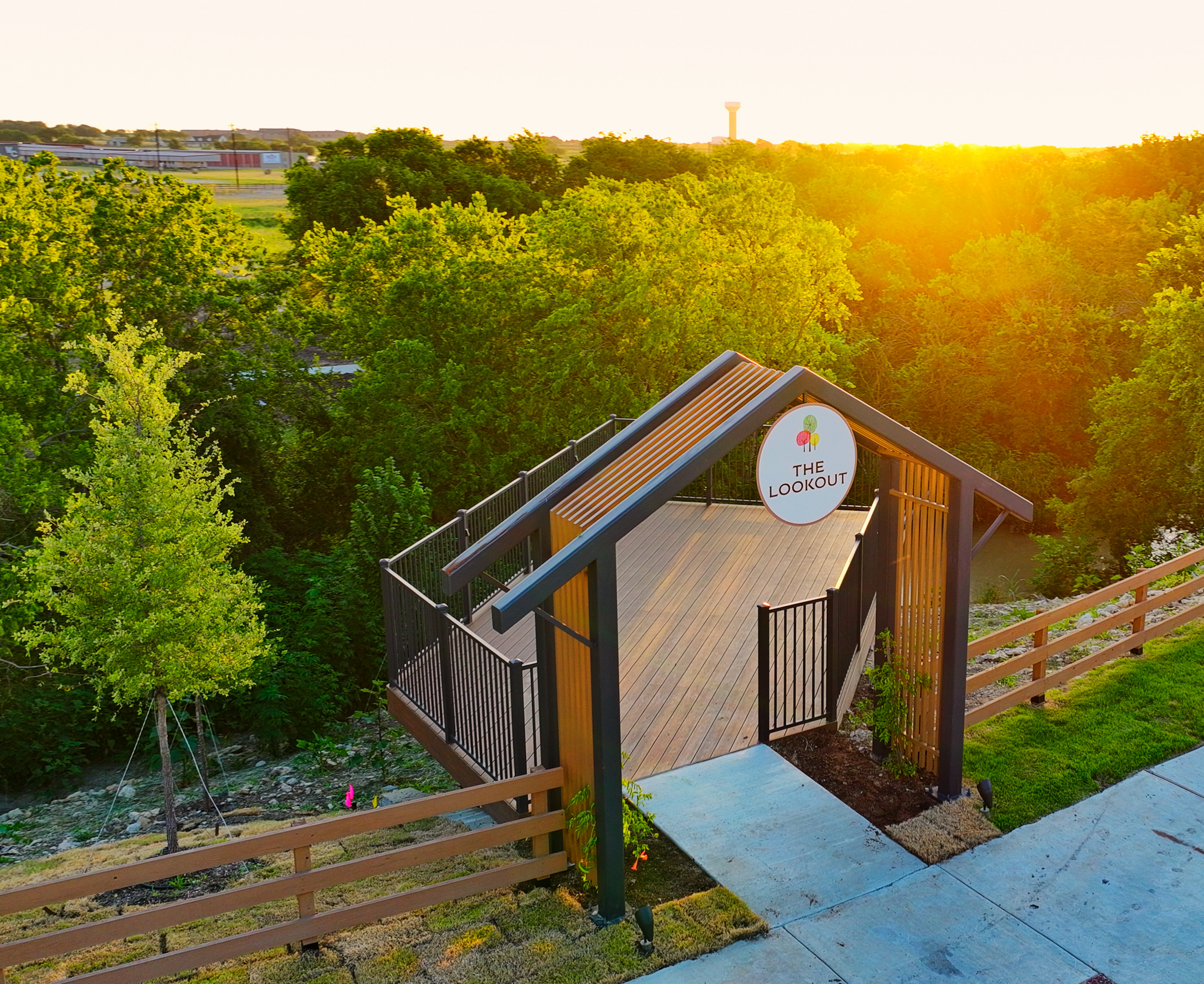 A wooden shed nestled among lush greenery, with a winding path leading towards a scenic backdrop of trees and buildings bathed in the warm glow of the setting sun.