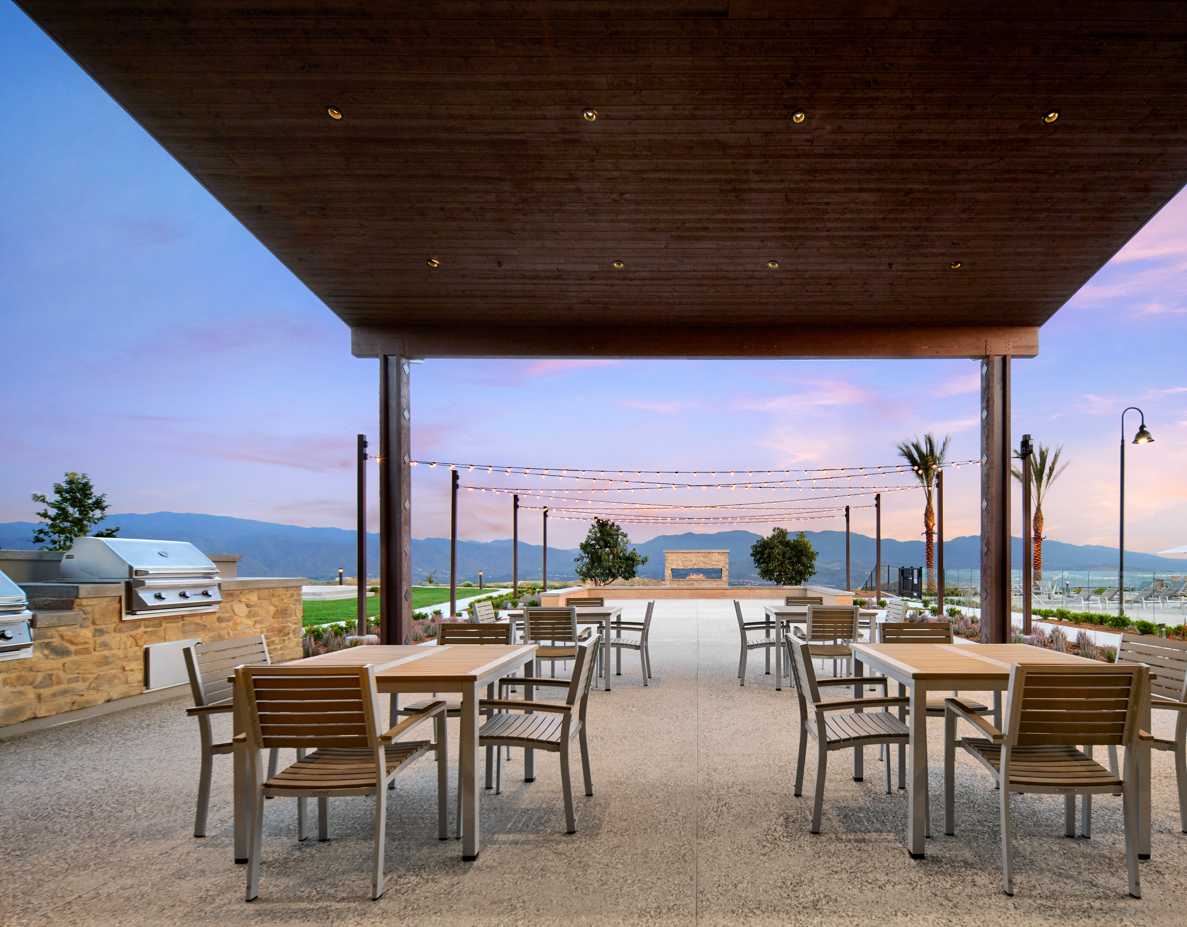 A covered outdoor dining area with wooden tables and chairs, overlooking a scenic landscape with mountains and a body of water in the background.