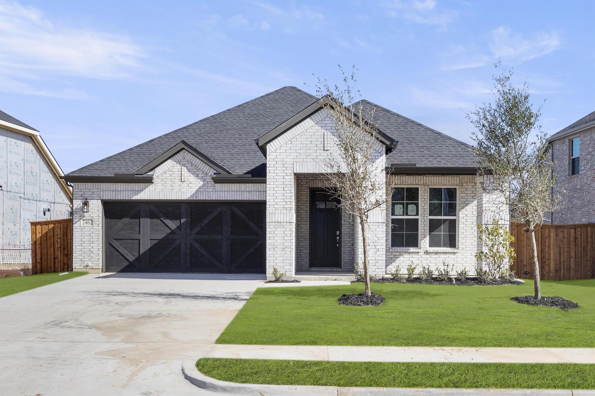 A two-story house with a gray roof, white exterior, and a well-manicured lawn in the foreground, set against a clear blue sky with some clouds.
