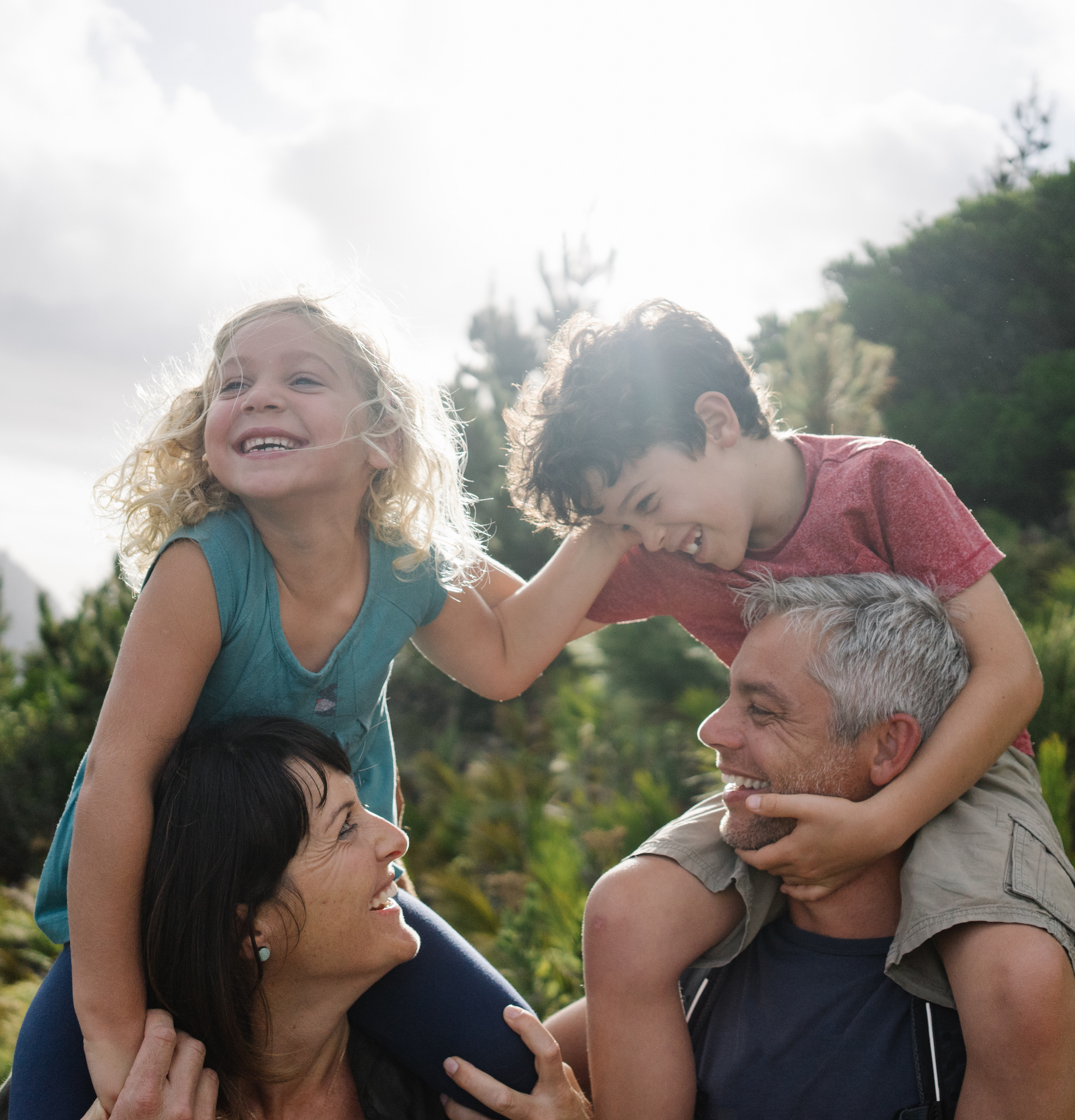 A family of four - two adults and two children - enjoying a moment together outdoors in a lush, forested setting.