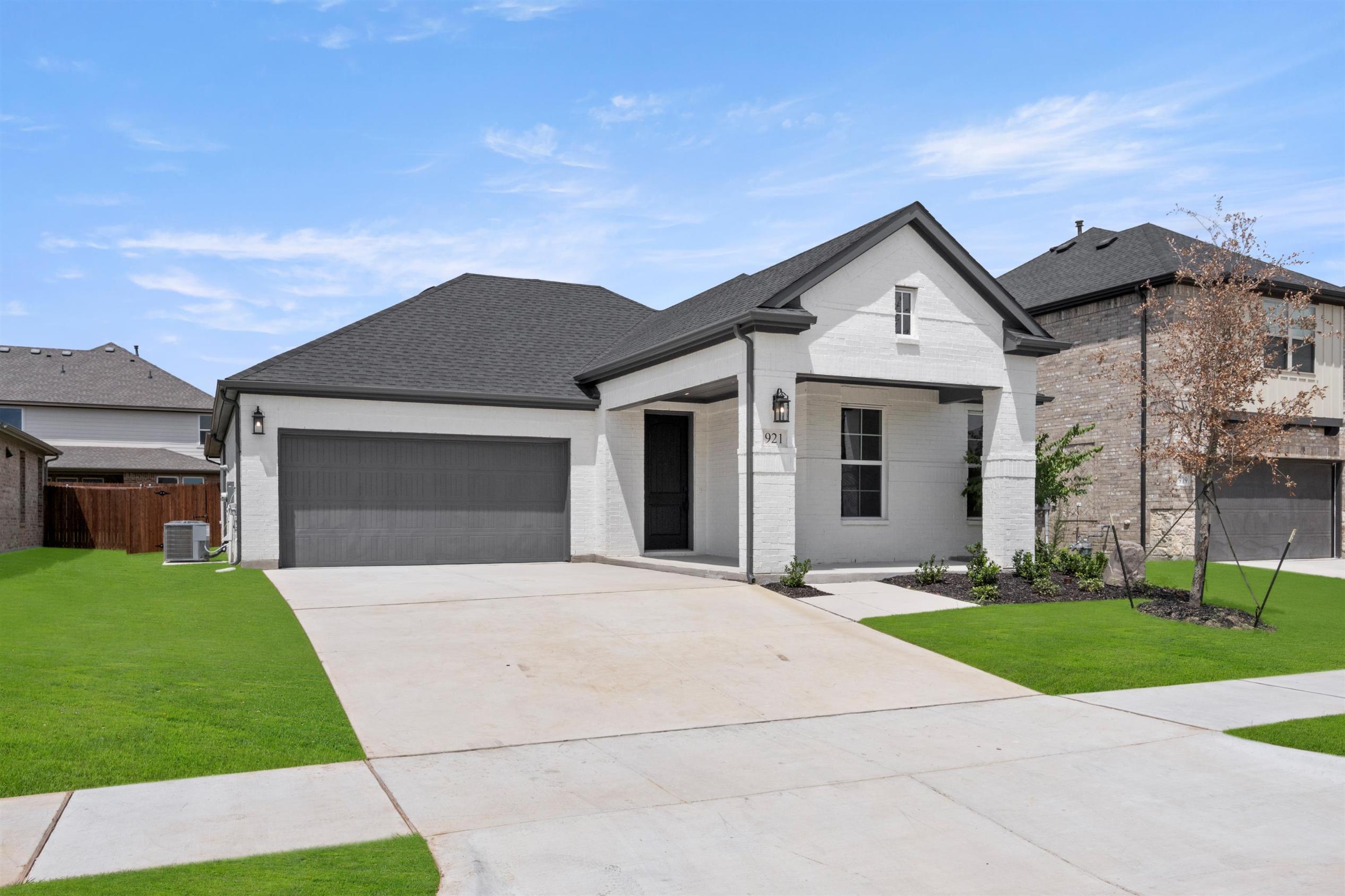 A modern two-story house with a gray roof and white exterior, surrounded by a well-manicured lawn and a paved driveway leading to a garage door.