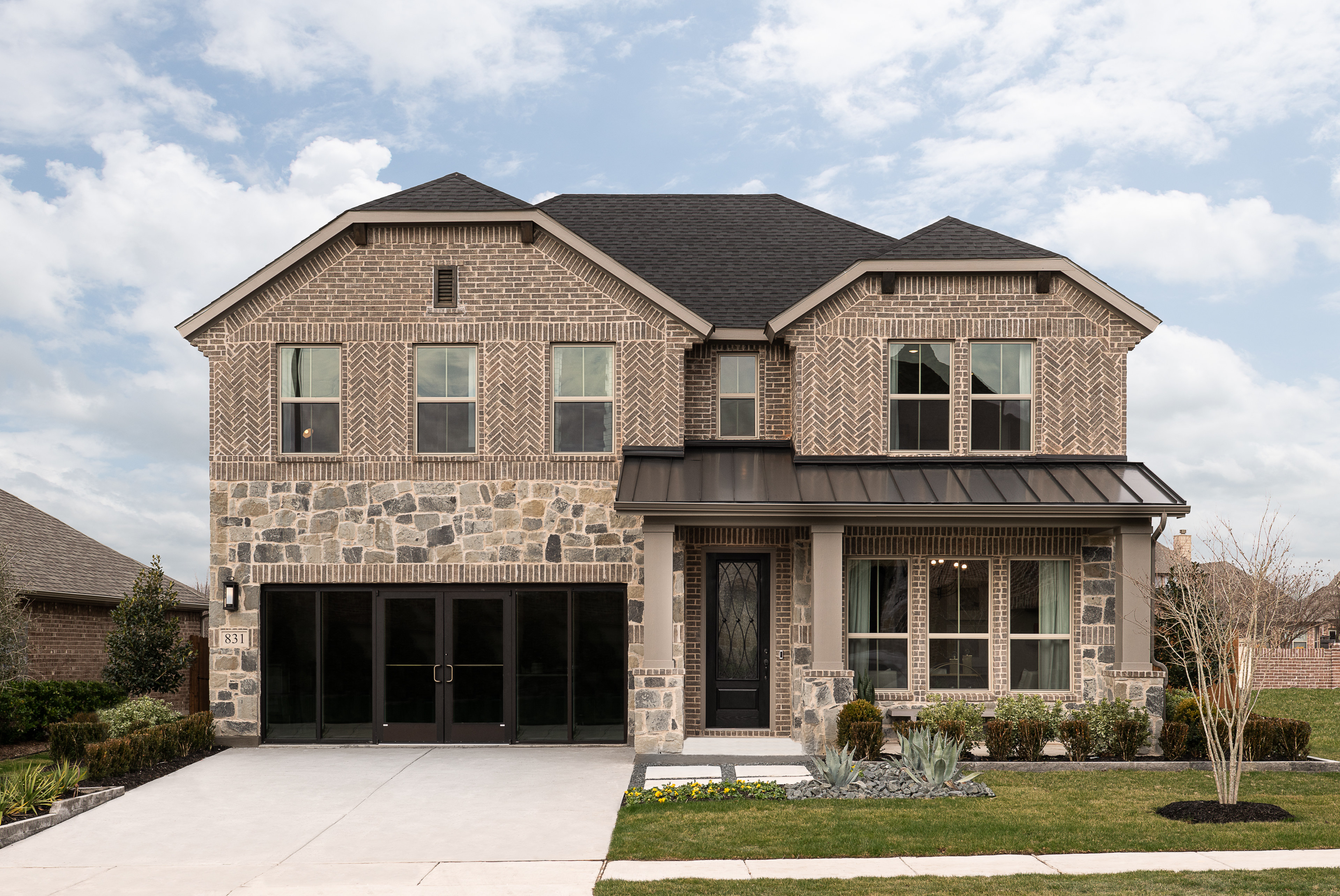 A two-story brick and stone house with a gabled roof, surrounded by a well-manicured lawn and landscaping, set against a cloudy sky.