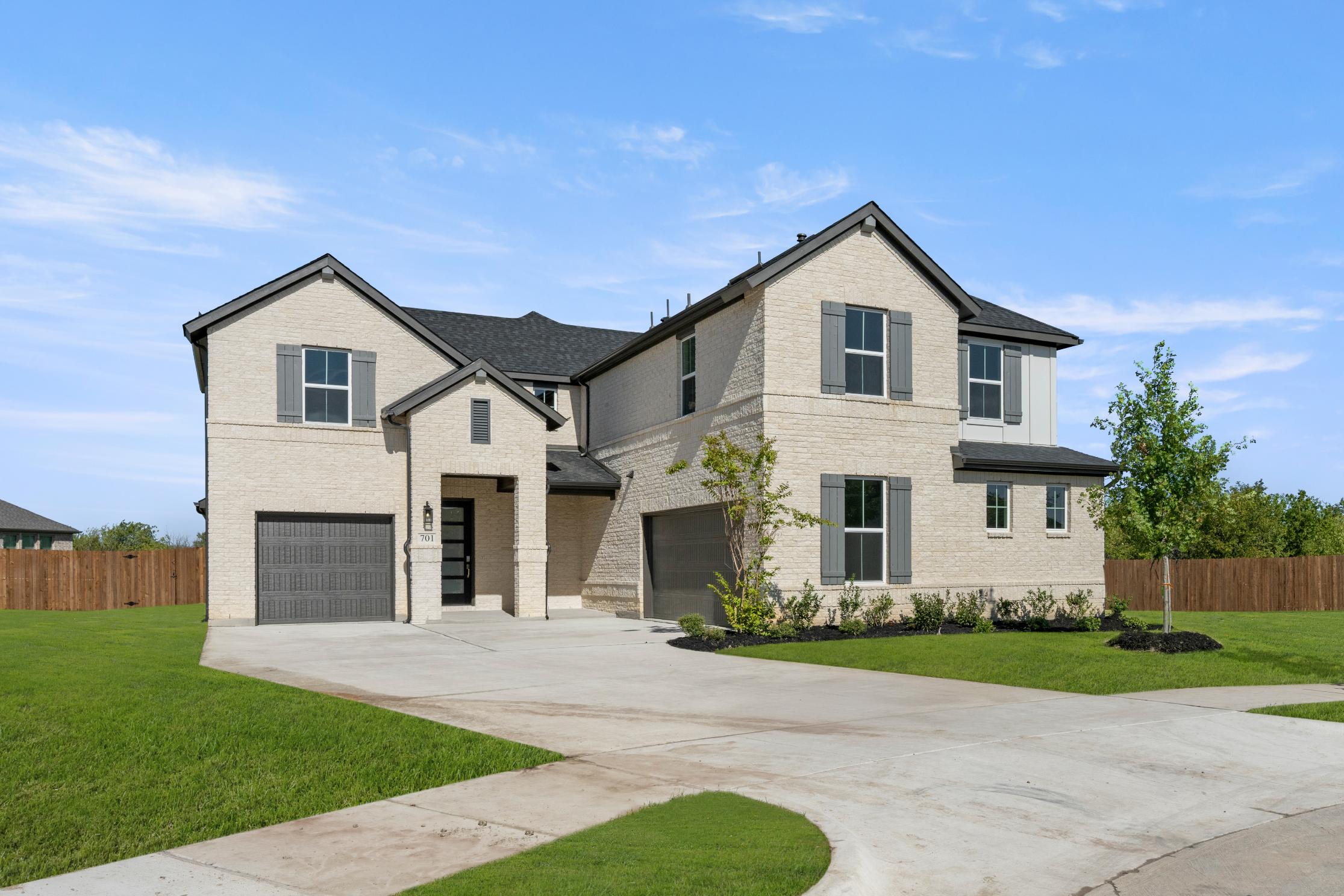 A two-story residential house with a garage, surrounded by a well-manicured lawn and a paved driveway, set against a clear blue sky with some clouds.