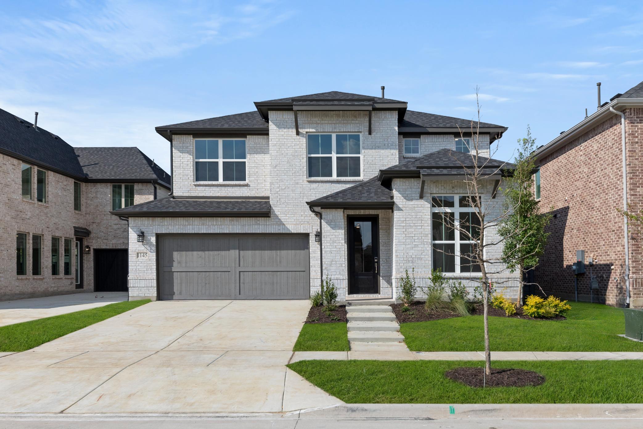 A two-story brick and stone house with a garage, surrounded by a well-manicured lawn and landscaping, set against a clear blue sky.