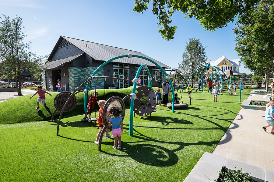 A colorful and vibrant playground with various play equipment, surrounded by lush greenery and a building in the background.