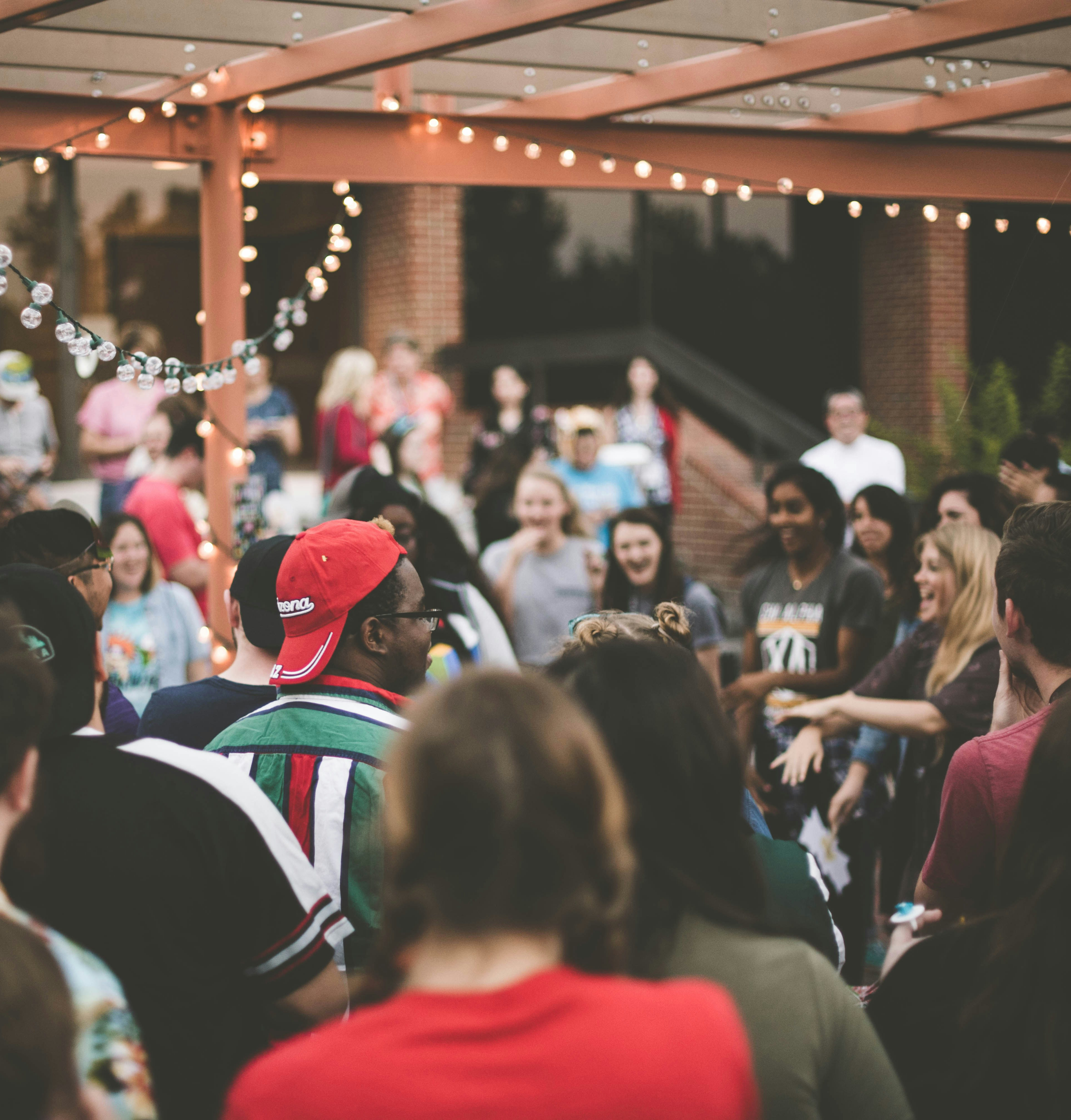 A crowded outdoor event with people gathered under string lights, creating a lively and festive atmosphere.