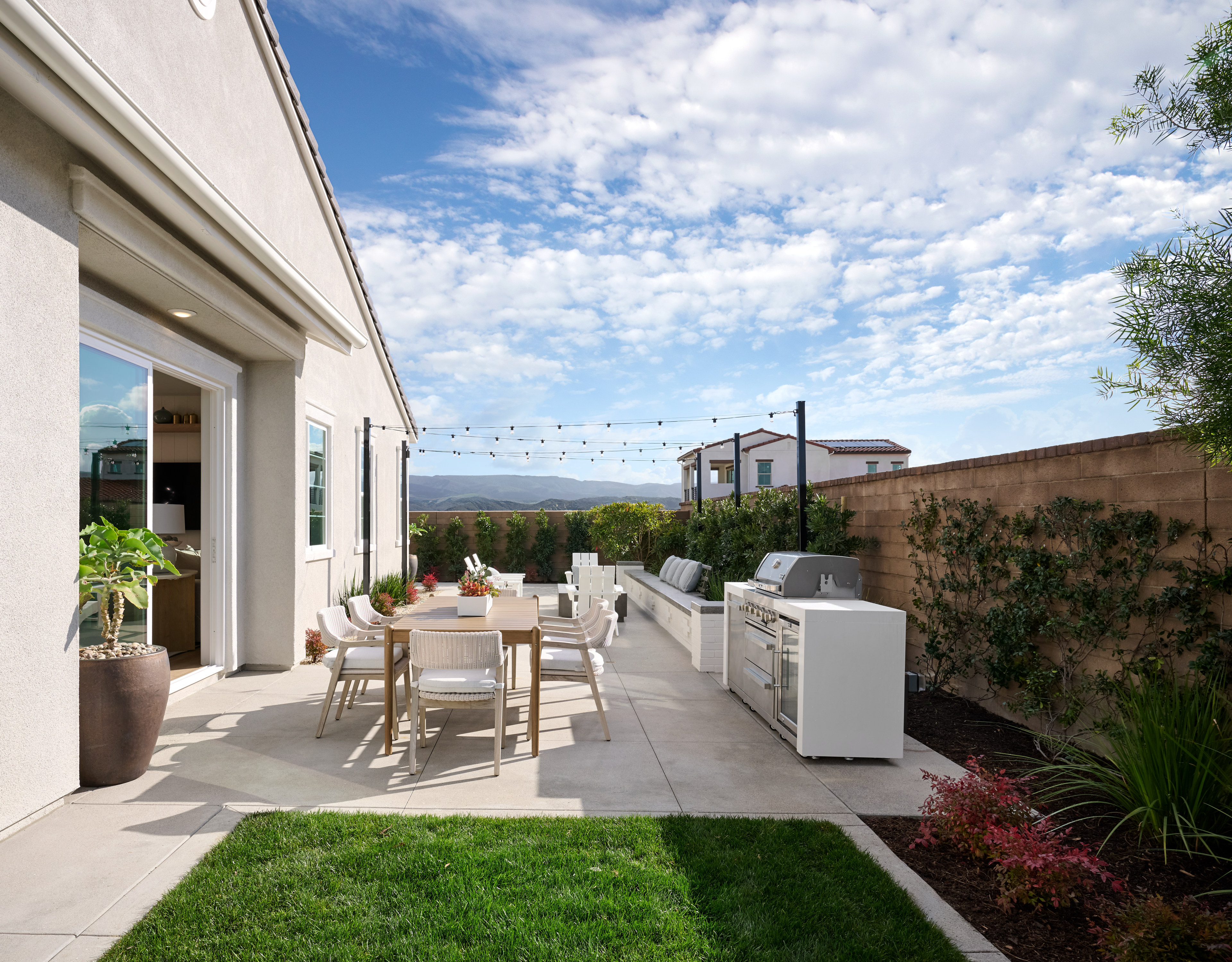 A well-designed outdoor living space with a patio, dining area, and landscaping, set against a backdrop of a clear blue sky with fluffy clouds.