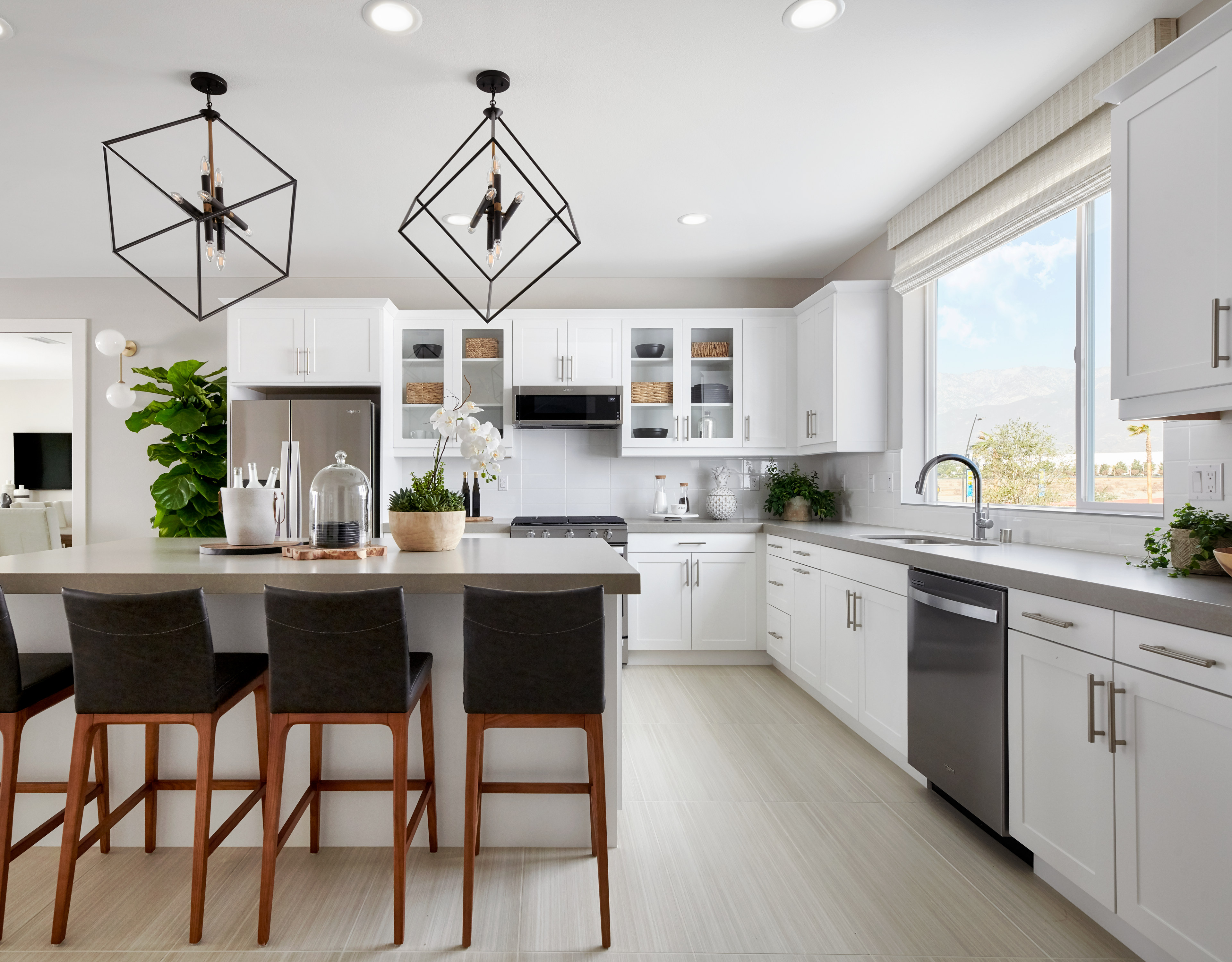 A modern, open-concept kitchen with white cabinets, stainless steel appliances, and a large island with bar stools, complemented by stylish pendant lighting fixtures.