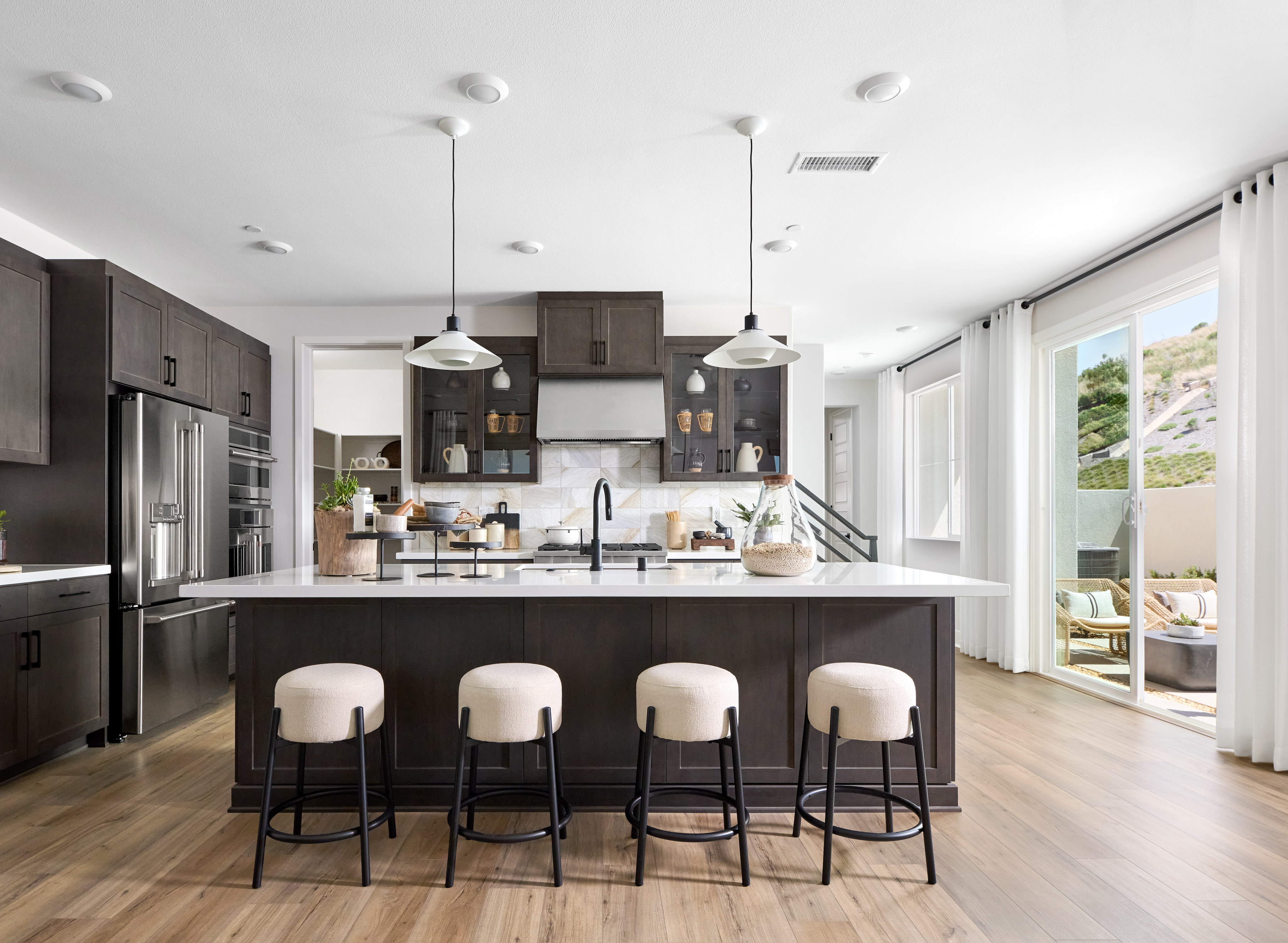 A modern and sleek kitchen with dark cabinets, a large island with bar stools, and a bright and airy atmosphere with large windows.