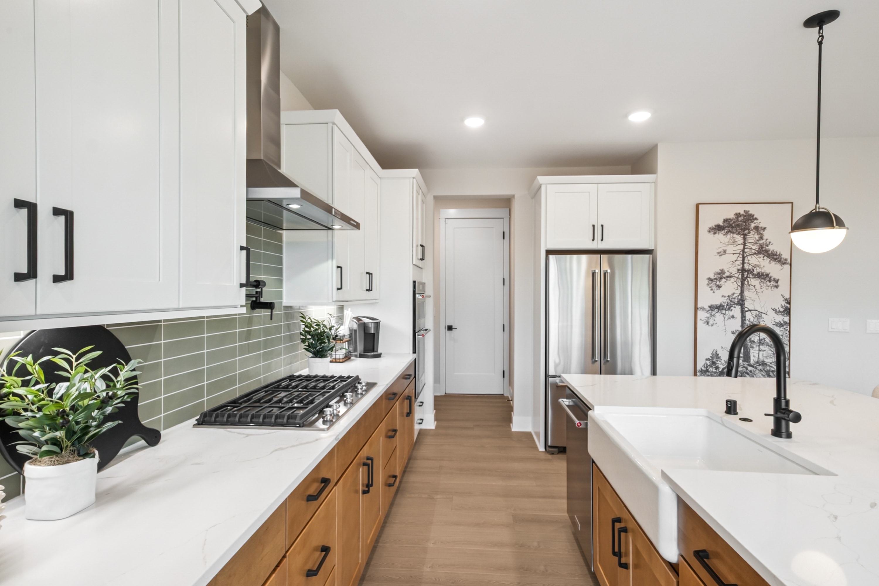A modern, well-designed kitchen with white cabinets, wooden countertops, and a green tile backsplash, featuring a large farmhouse-style sink and various appliances and decor elements.