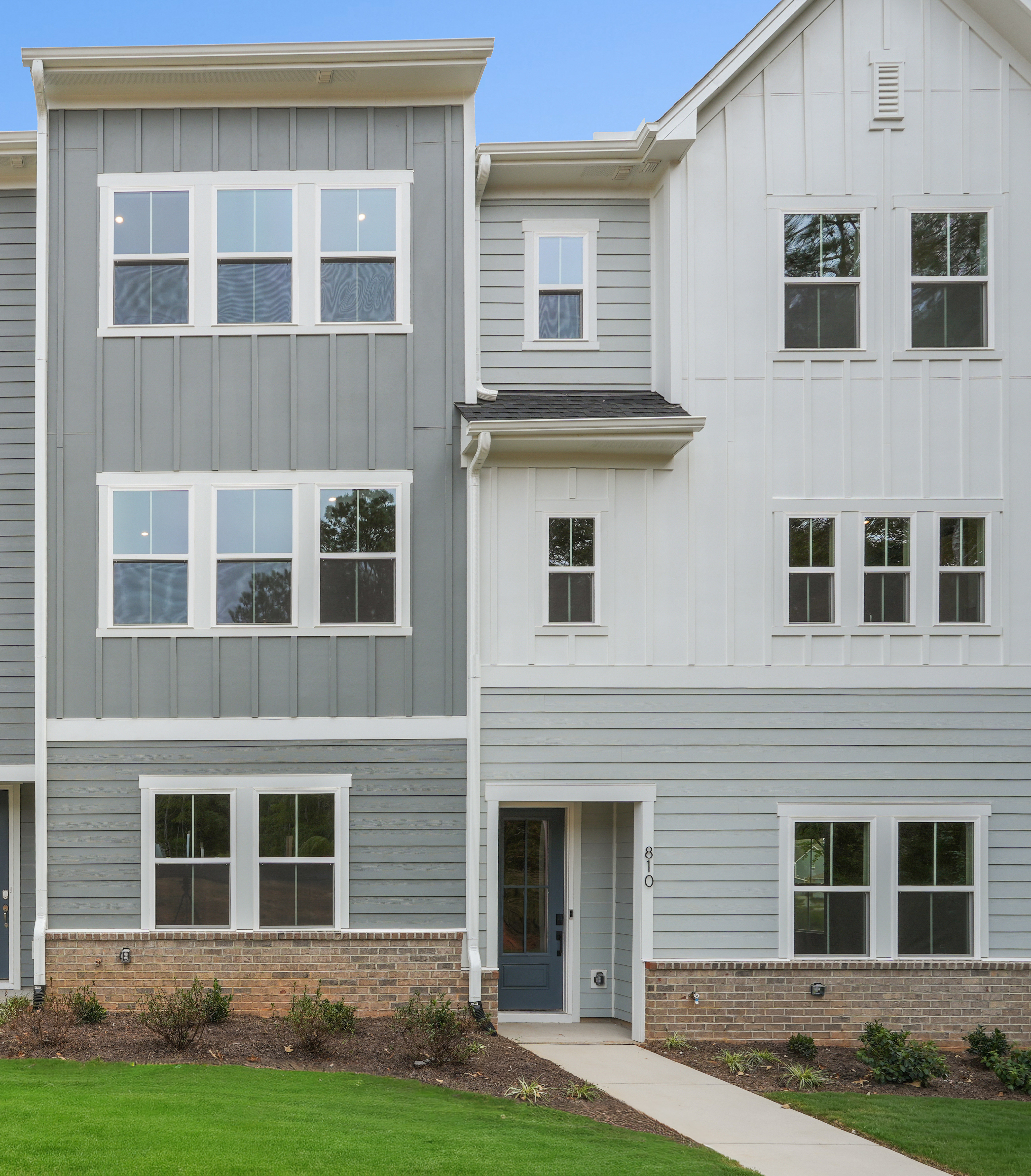 The image depicts a modern, multi-story townhouse complex with a well-manicured lawn in the foreground.