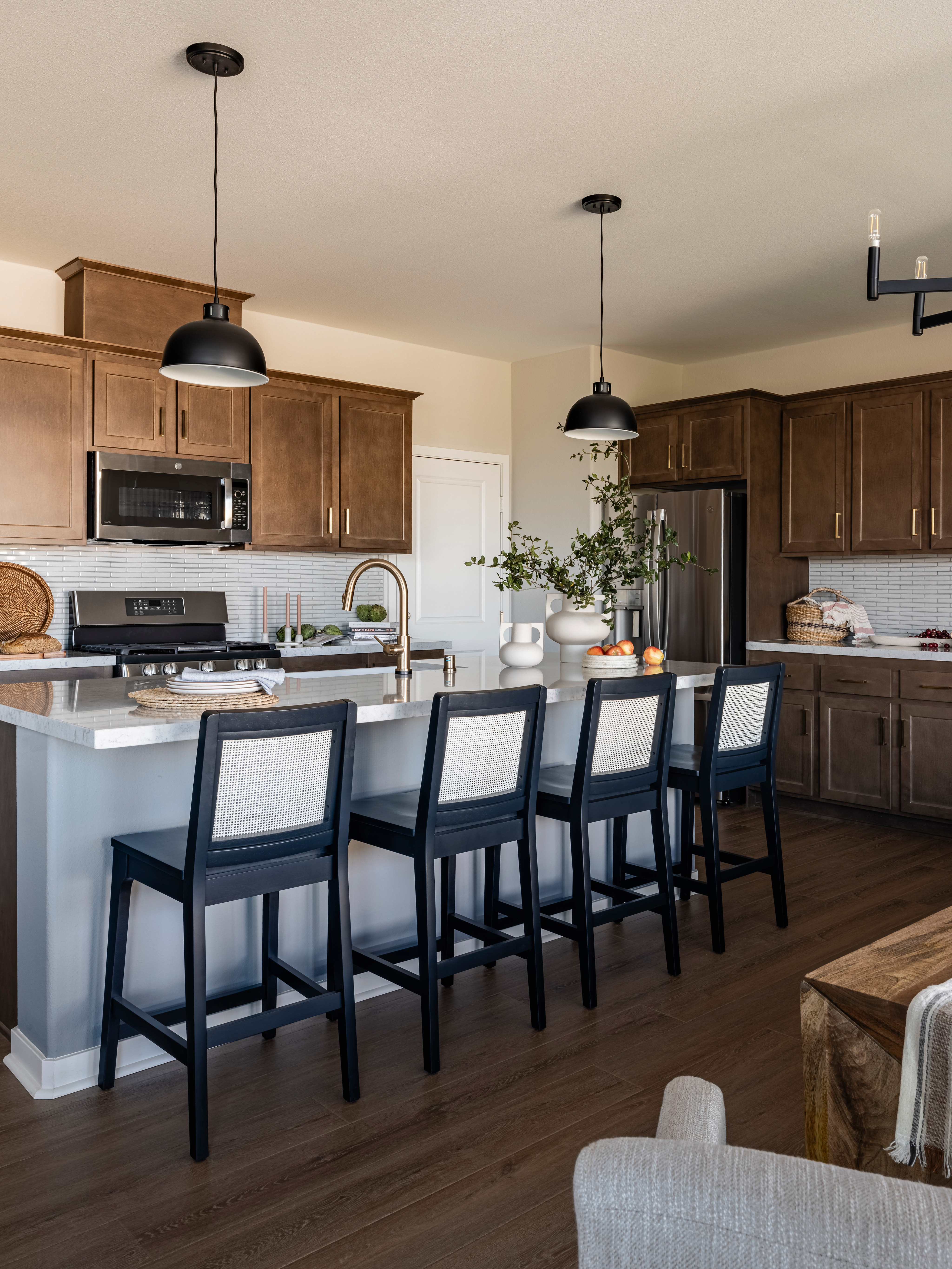 A modern and spacious kitchen with wooden cabinets, a large island with bar stools, and a chandelier overhead, set against a backdrop of a dining area with a table and chairs.