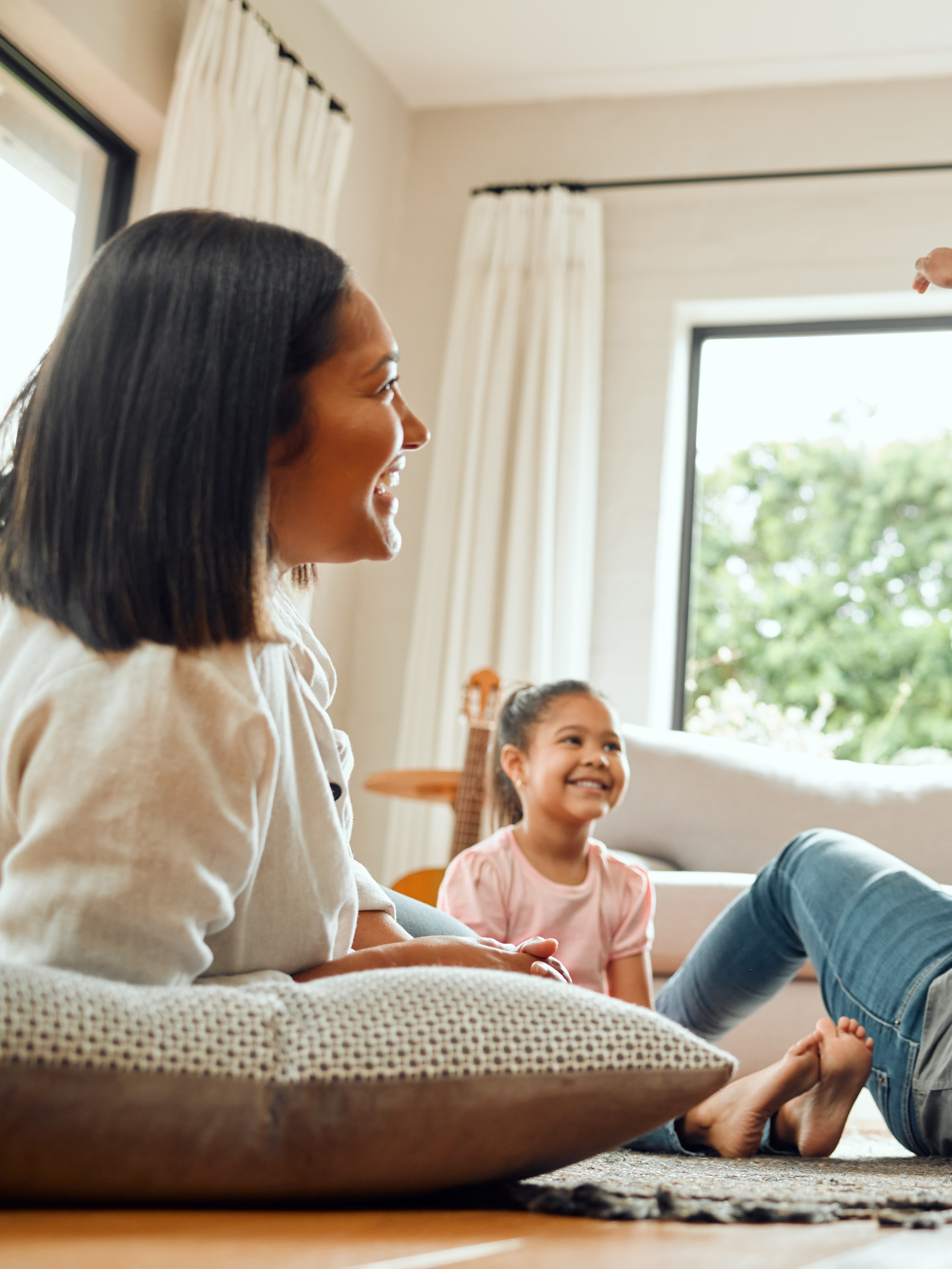 A family enjoying quality time together, with a young child playfully jumping on a parent lying on the floor, while another child sits nearby on a couch.