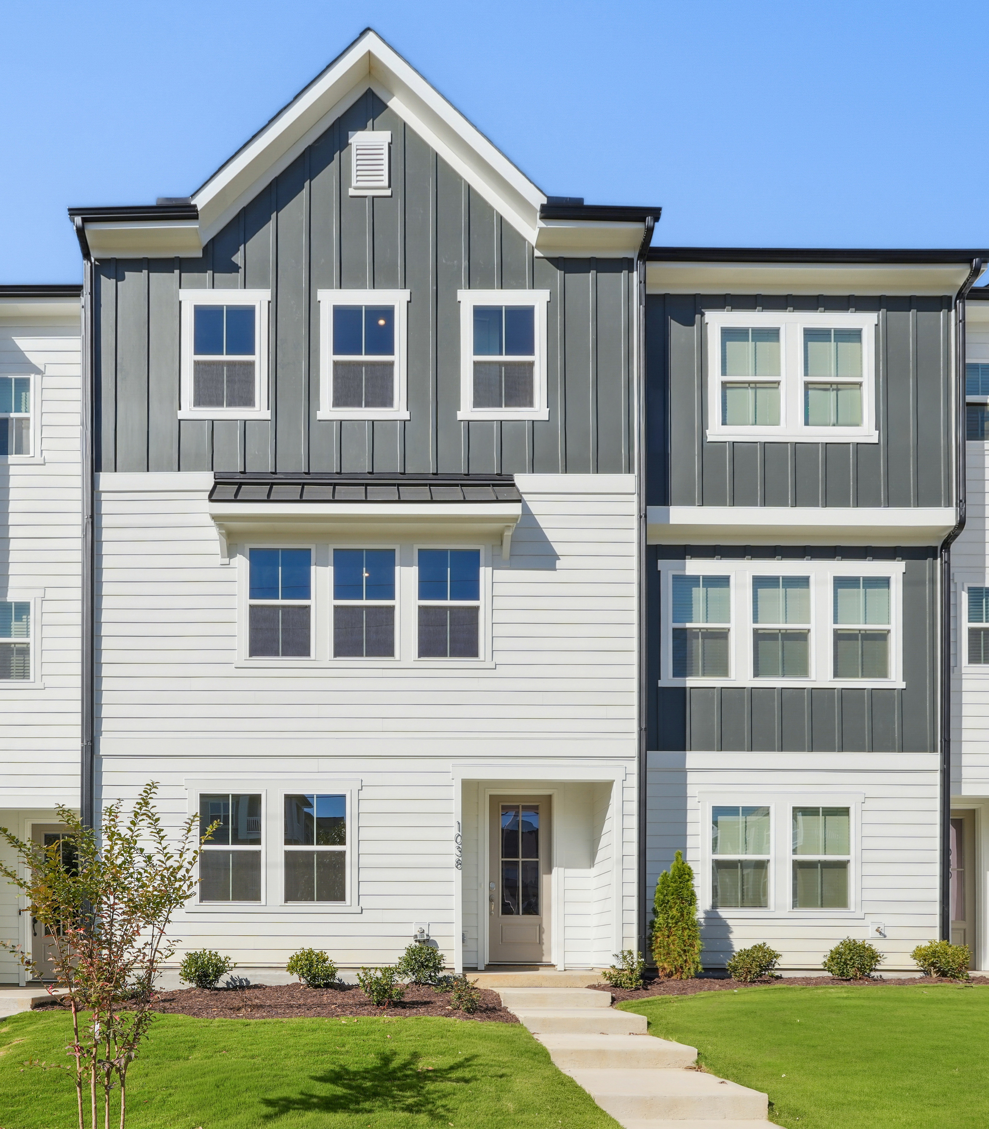 A multi-story residential building with a gray and white exterior, surrounded by a well-manicured lawn and landscaping.