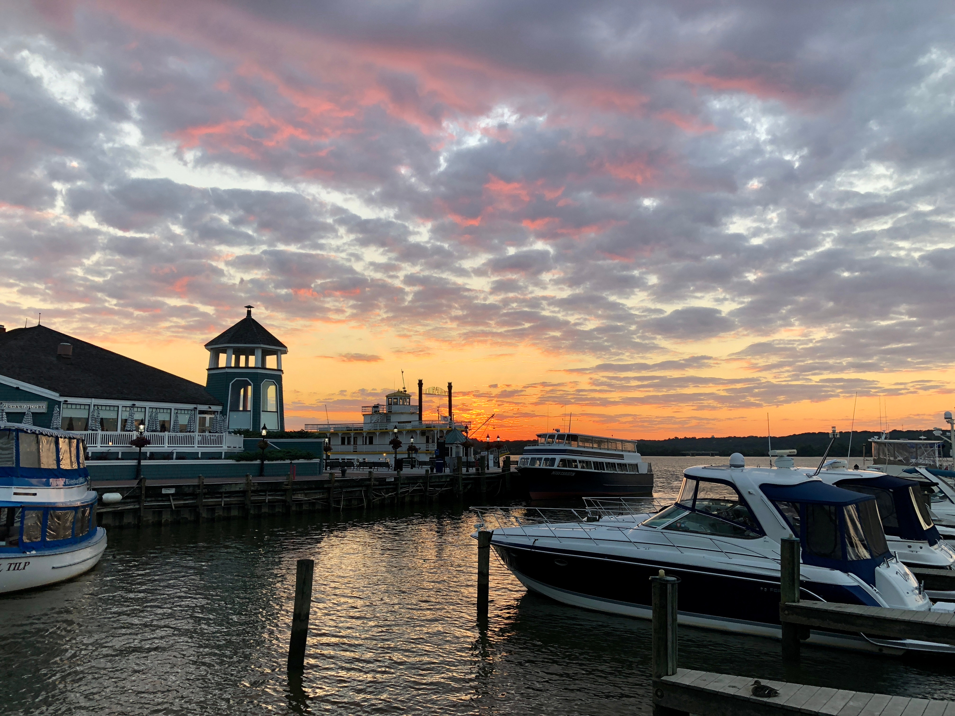 A picturesque harbor scene with boats docked along the waterfront, set against a dramatic sky filled with vibrant hues of orange and pink at sunset.
