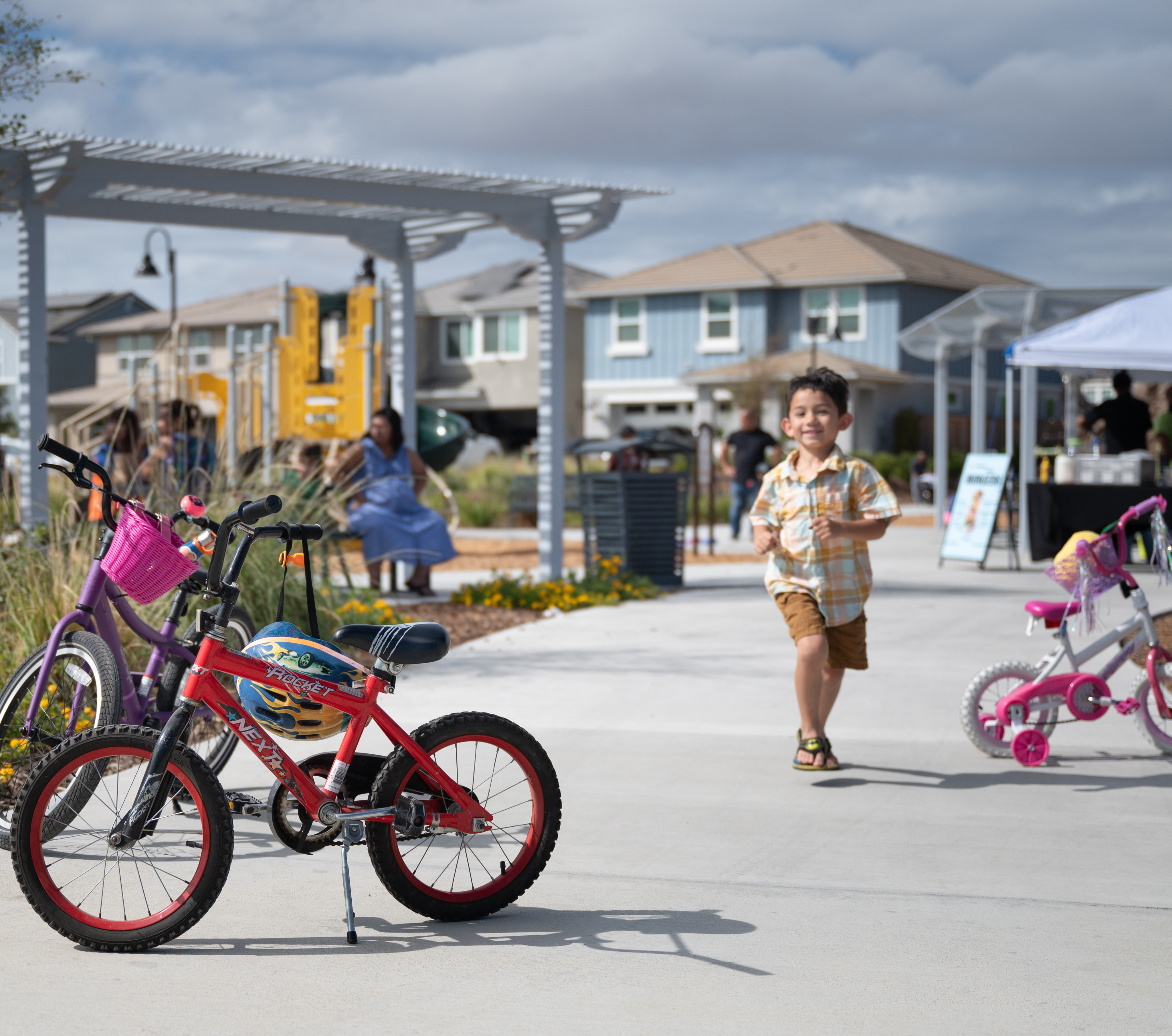 A vibrant outdoor shopping area with colorful bicycles and children playing in the foreground, surrounded by various shops and buildings in the background.
