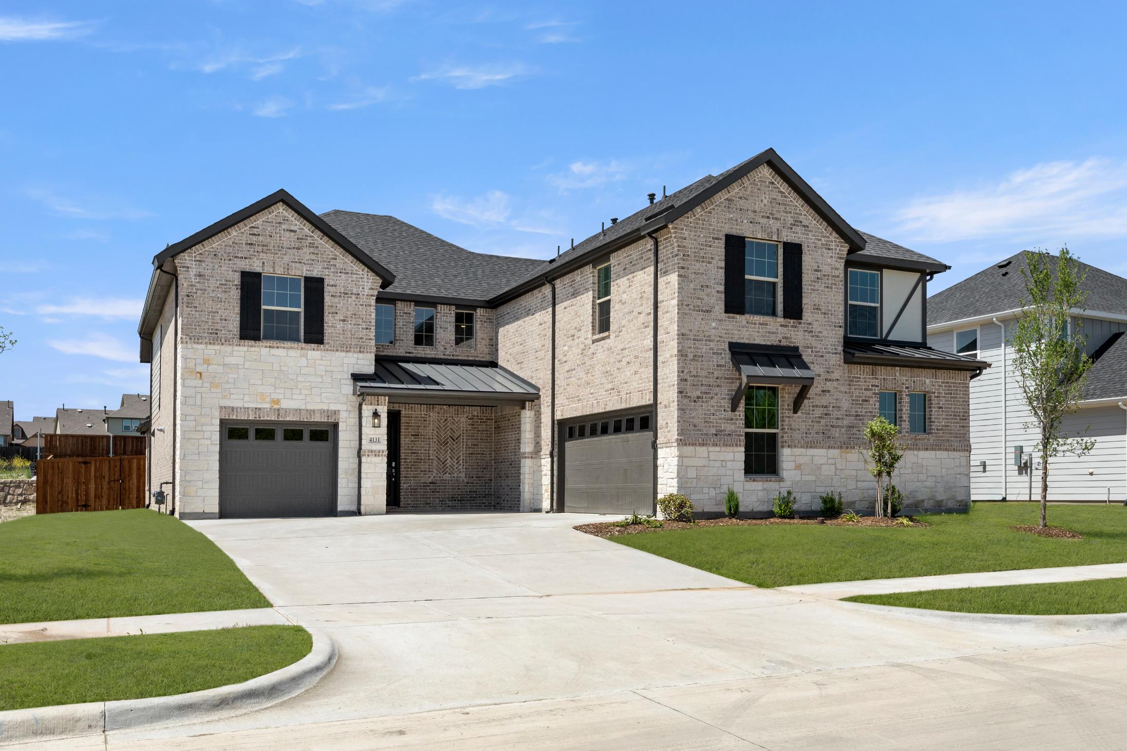 A large, two-story brick house with a garage and a well-manicured lawn in the foreground, set against a clear blue sky with some clouds.